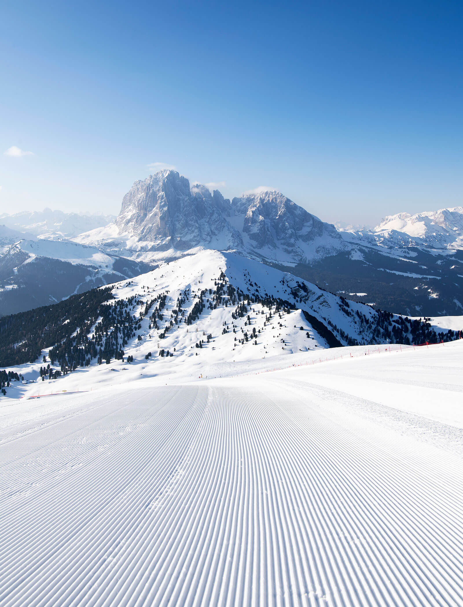 Pista da sci innevata e battuta, con linee parallele, una catena montuosa e il cielo azzurro sullo sfondo. - Hotel Kristiania