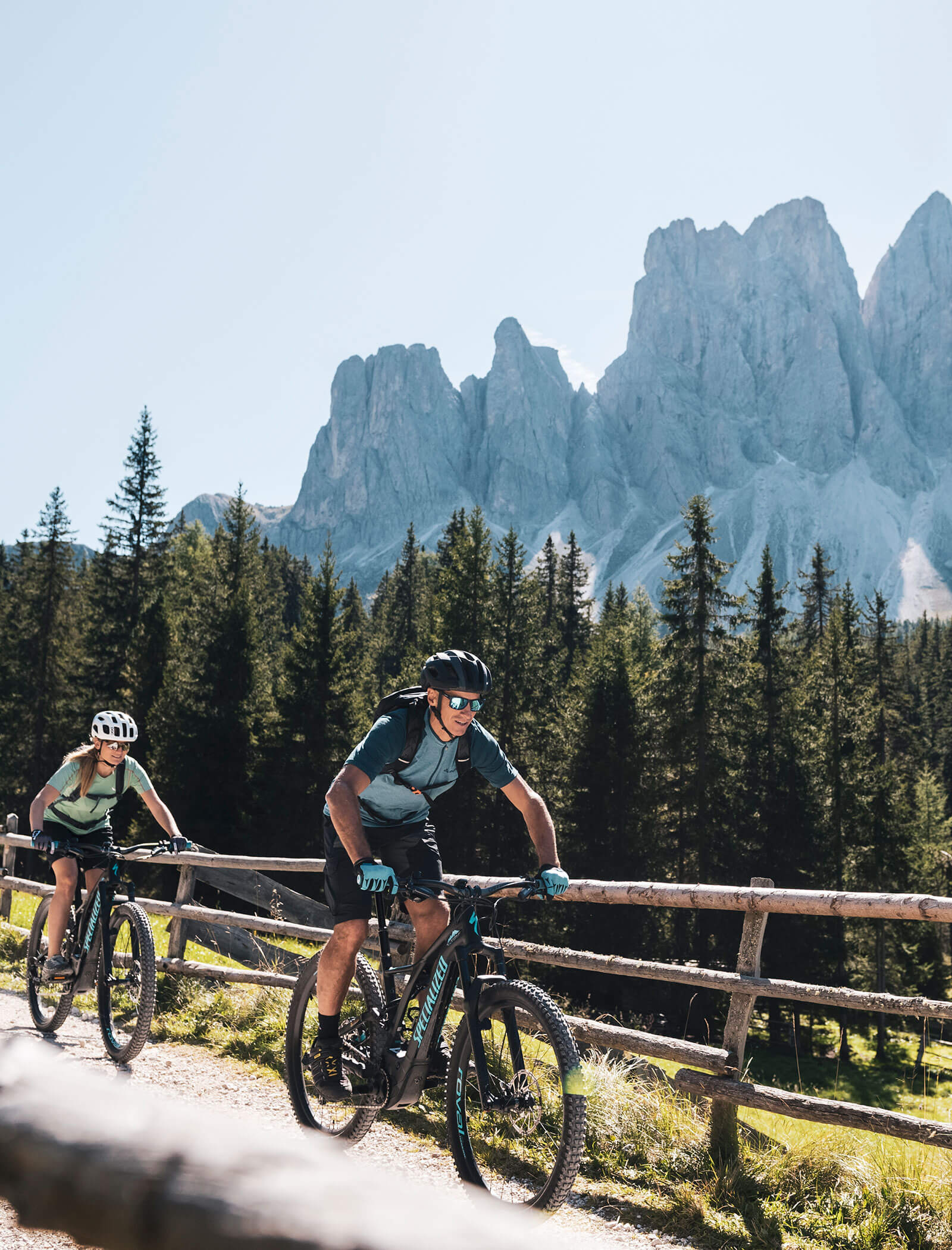 Zwei Radfahrer fahren mit ihren Mountainbikes auf einem Feldweg, im Hintergrund sind hohe Kiefern und felsige Berge zu sehen. - Hotel Kristiania