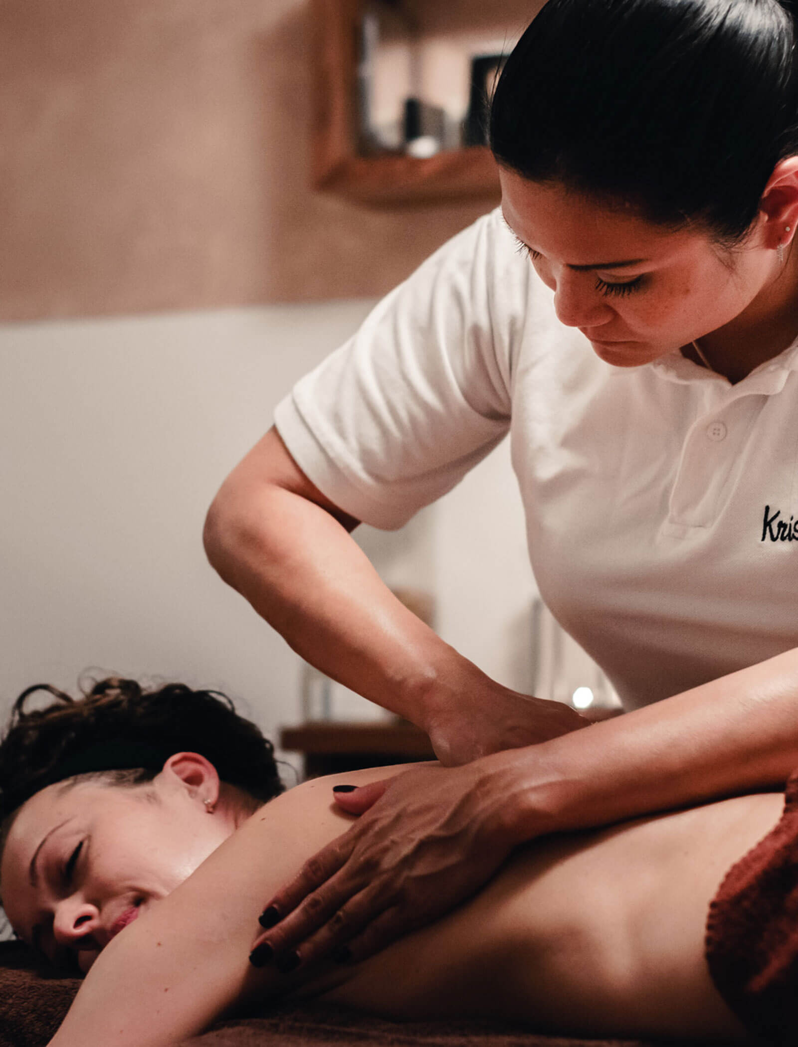 A woman receives a back massage from a therapist in a white polo shirt in a spa setting. - Hotel Kristiania