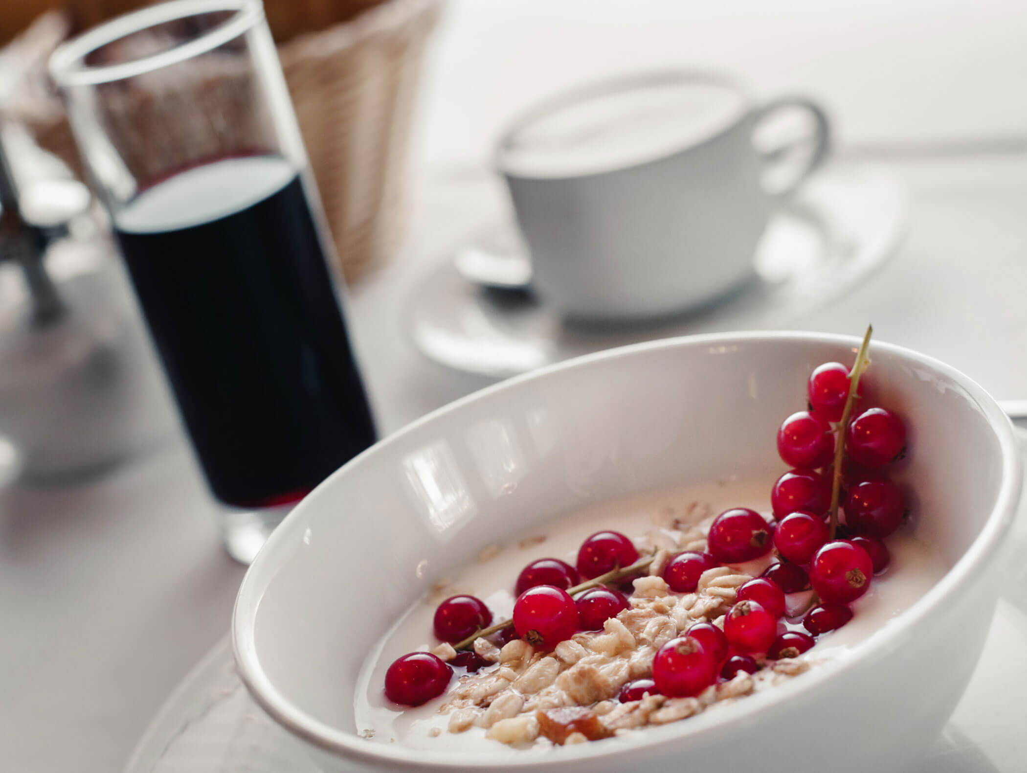 A bowl of cereal with milk, walnuts, and red currants next to a cup of coffee and a glass of juice. - Hotel Kristiania
