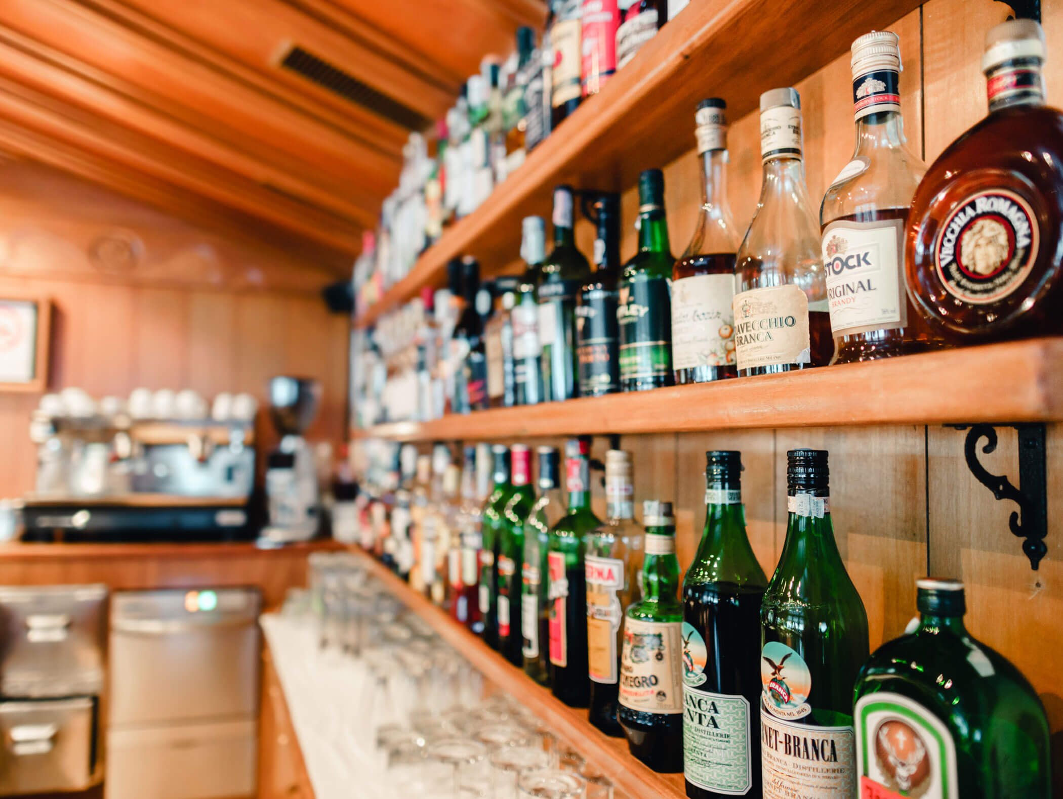 Bottles of liquor and spirits arranged on wooden shelves in a bar with glasses lined up below. - Hotel Kristiania