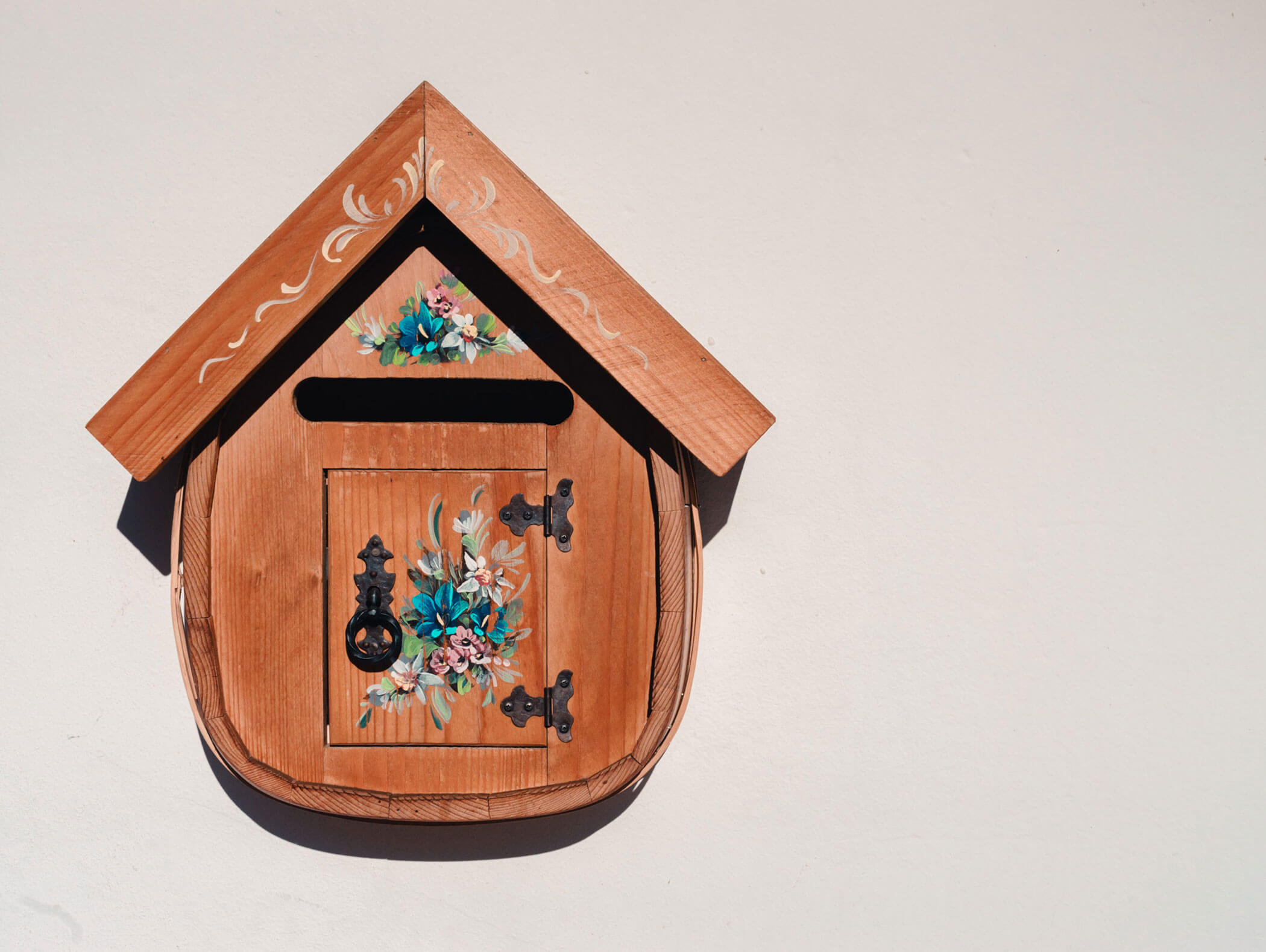 Wooden mailbox with a small door and floral decorations, mounted on a plain white wall. - Hotel Kristiania