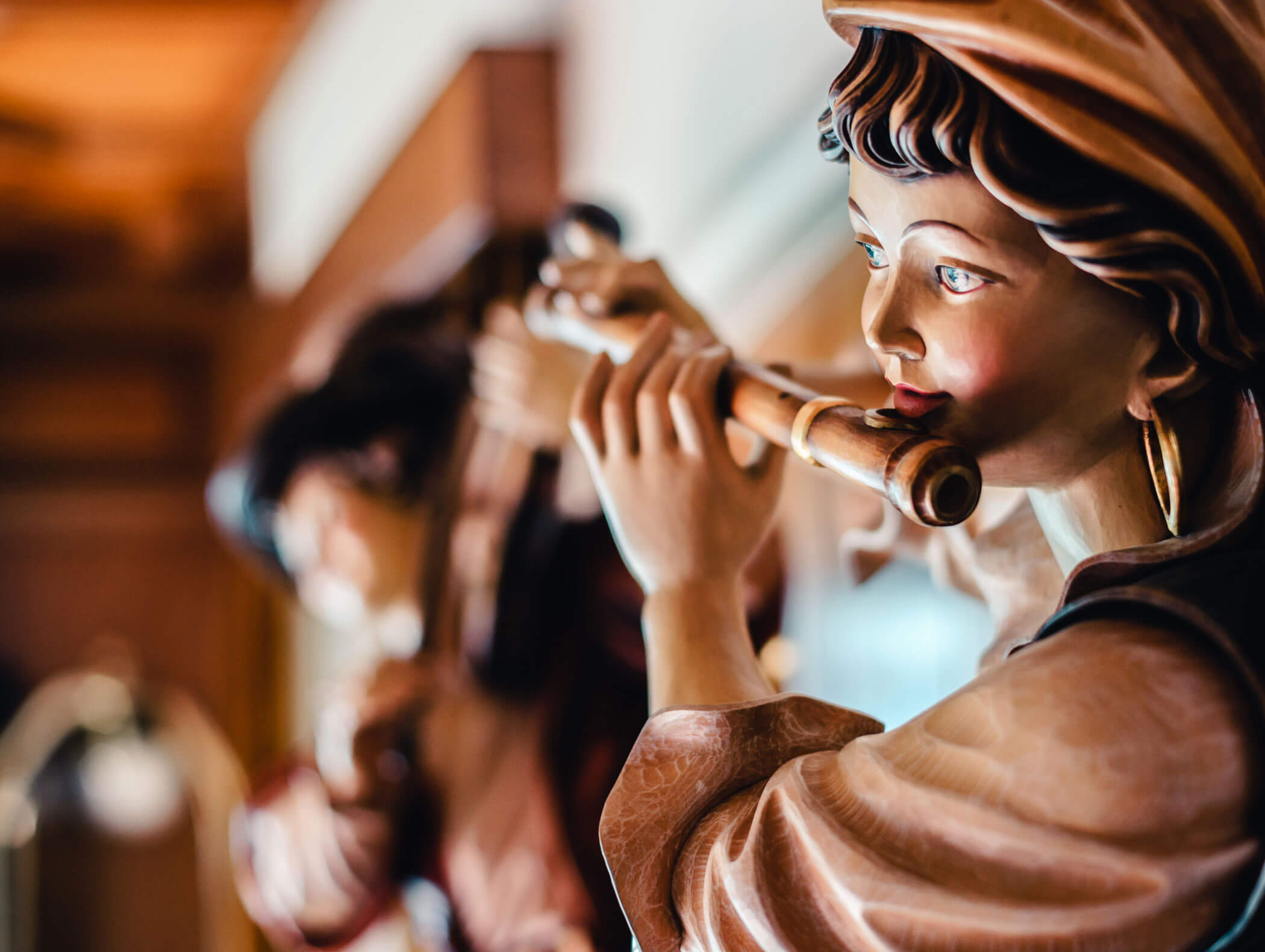 Close-up of a painted wooden statue playing a flute, with another musician statue blurred in the background. - Hotel Kristiania