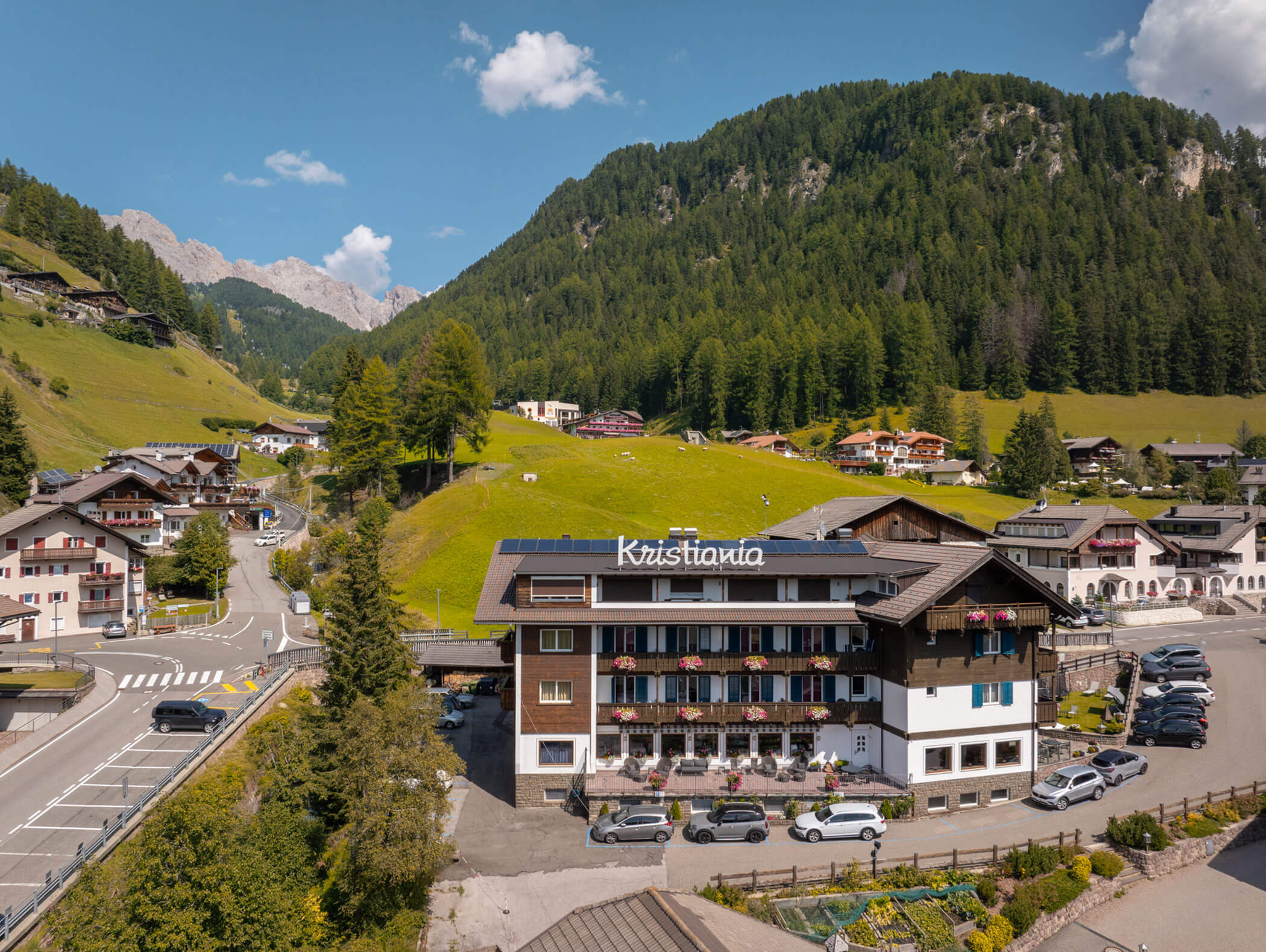 Hotel Kristania nestled among lush green hills and pine forests in a scenic mountain village. - Hotel Kristiania