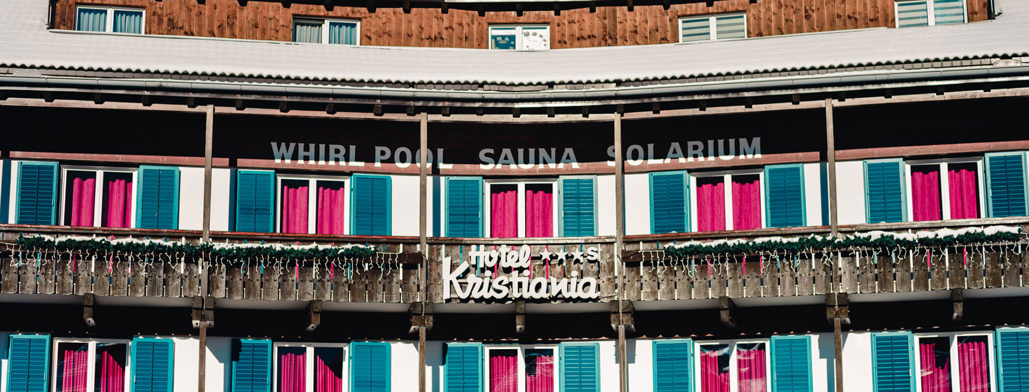 Hotel facade with blue shutters, pink curtains, and signs reading WHIRL POOL SAUNA SOLARIUM and Kristallinia. - Hotel Kristiania