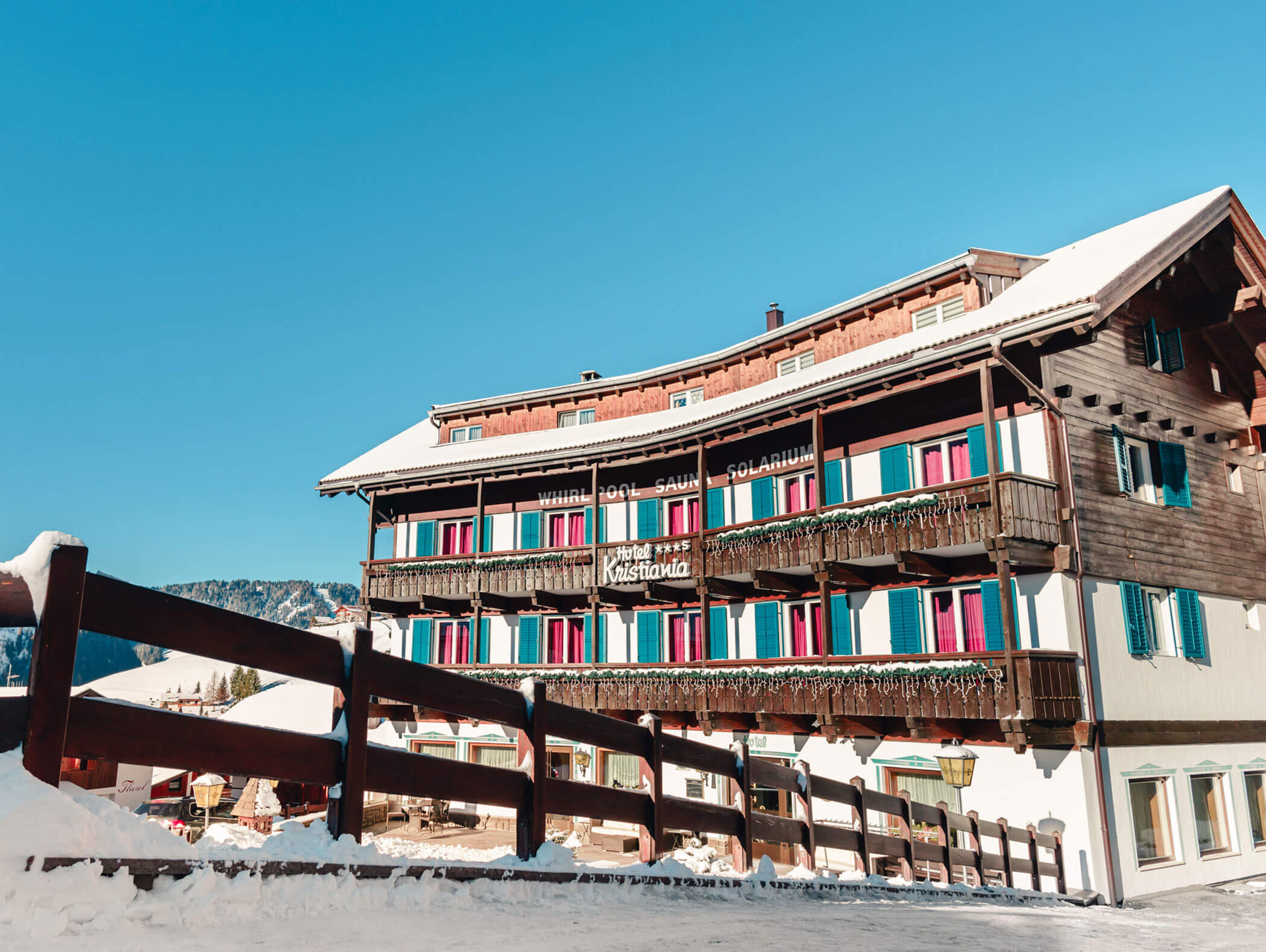 Alpine hotel with blue and red shutters, snow-covered roof, and clear blue sky in the background. - Hotel Kristiania