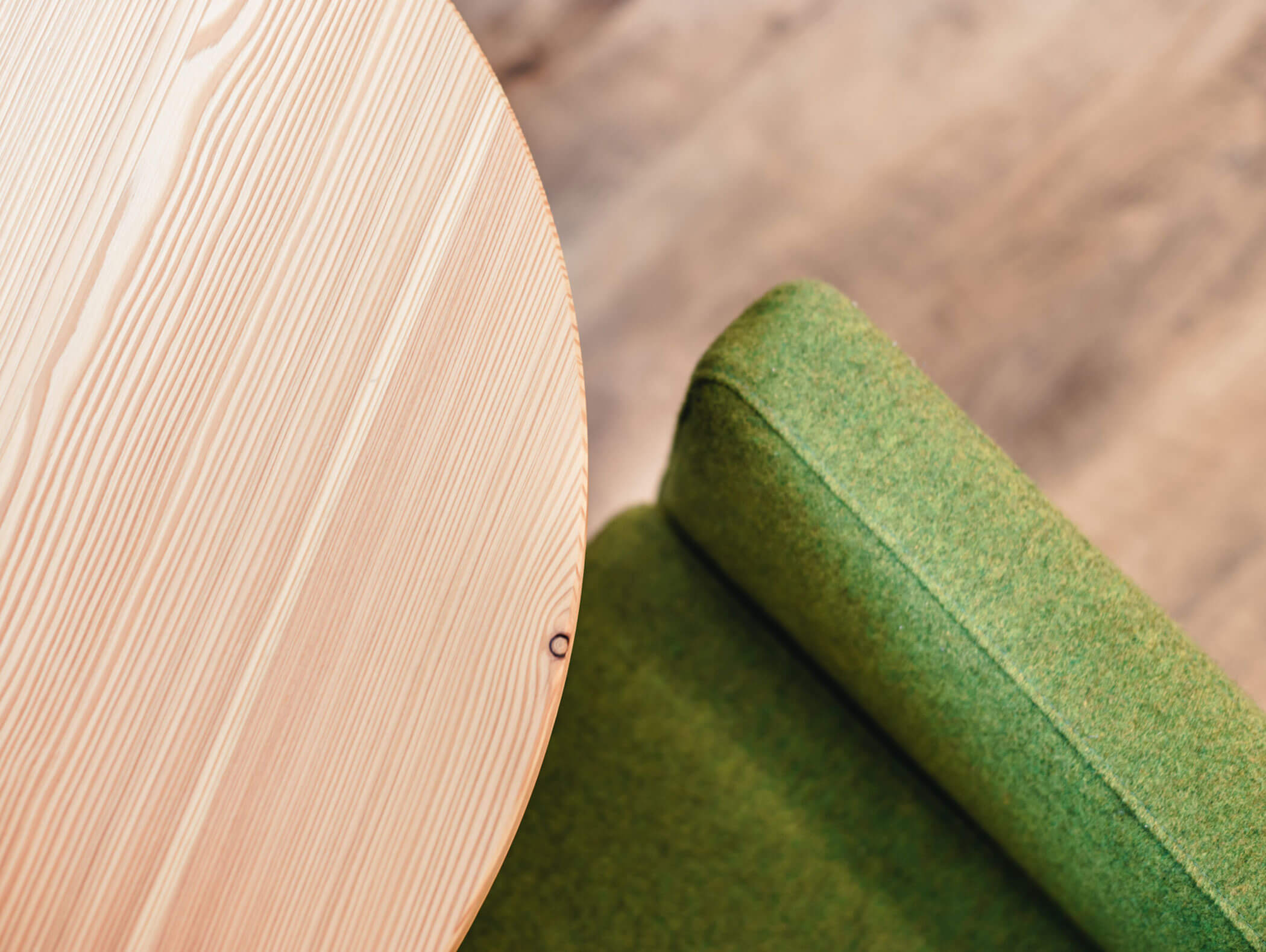 Close-up of a round wooden table next to a green upholstered chair on a wooden floor. - Hotel Kristiania