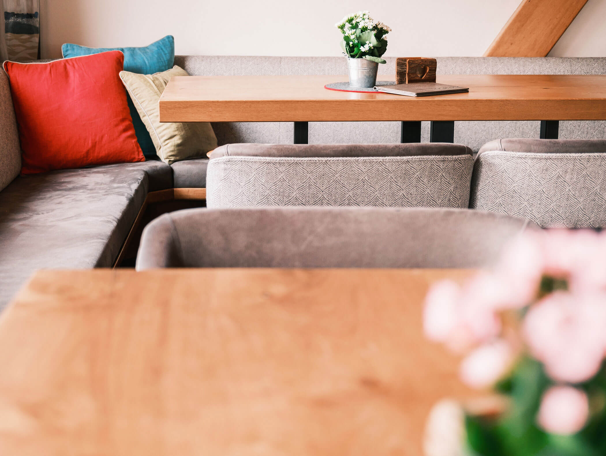 A cozy cafe corner with colorful cushions, a wooden table, and potted flowers on the tables. - Hotel Kristiania