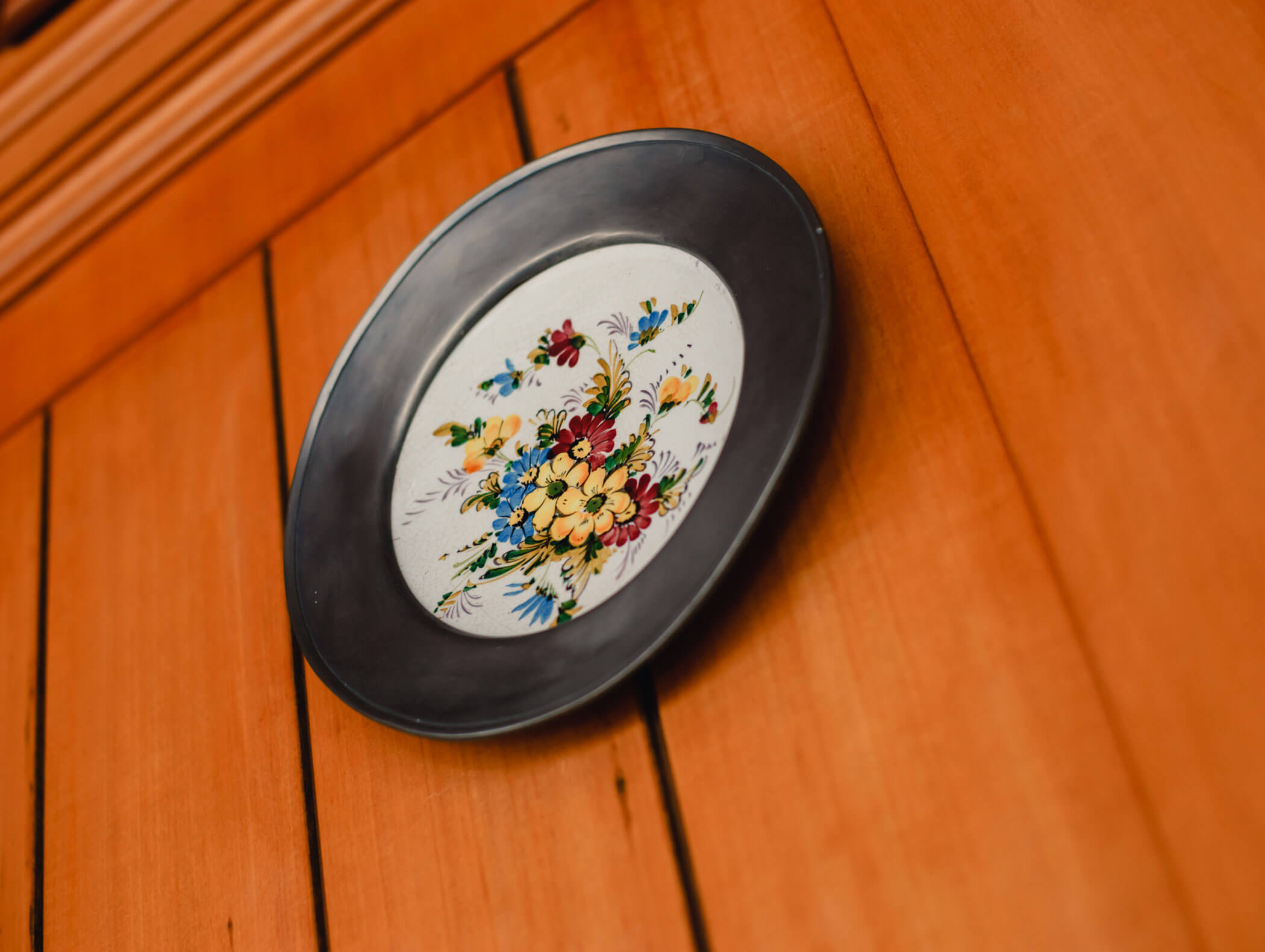 Decorative plate with a colorful floral design hanging on a wooden paneled wall. - Hotel Kristiania
