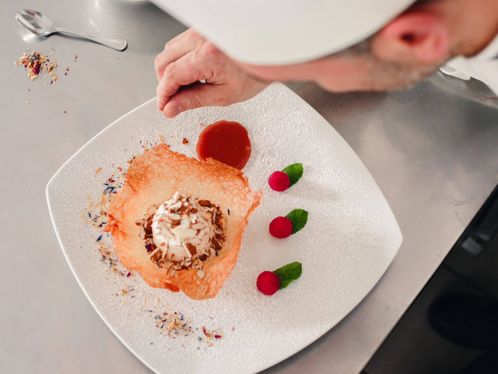 A chef decorates a gourmet dessert with sauce, raspberries, and mint on a white plate. - Hotel Kristiania