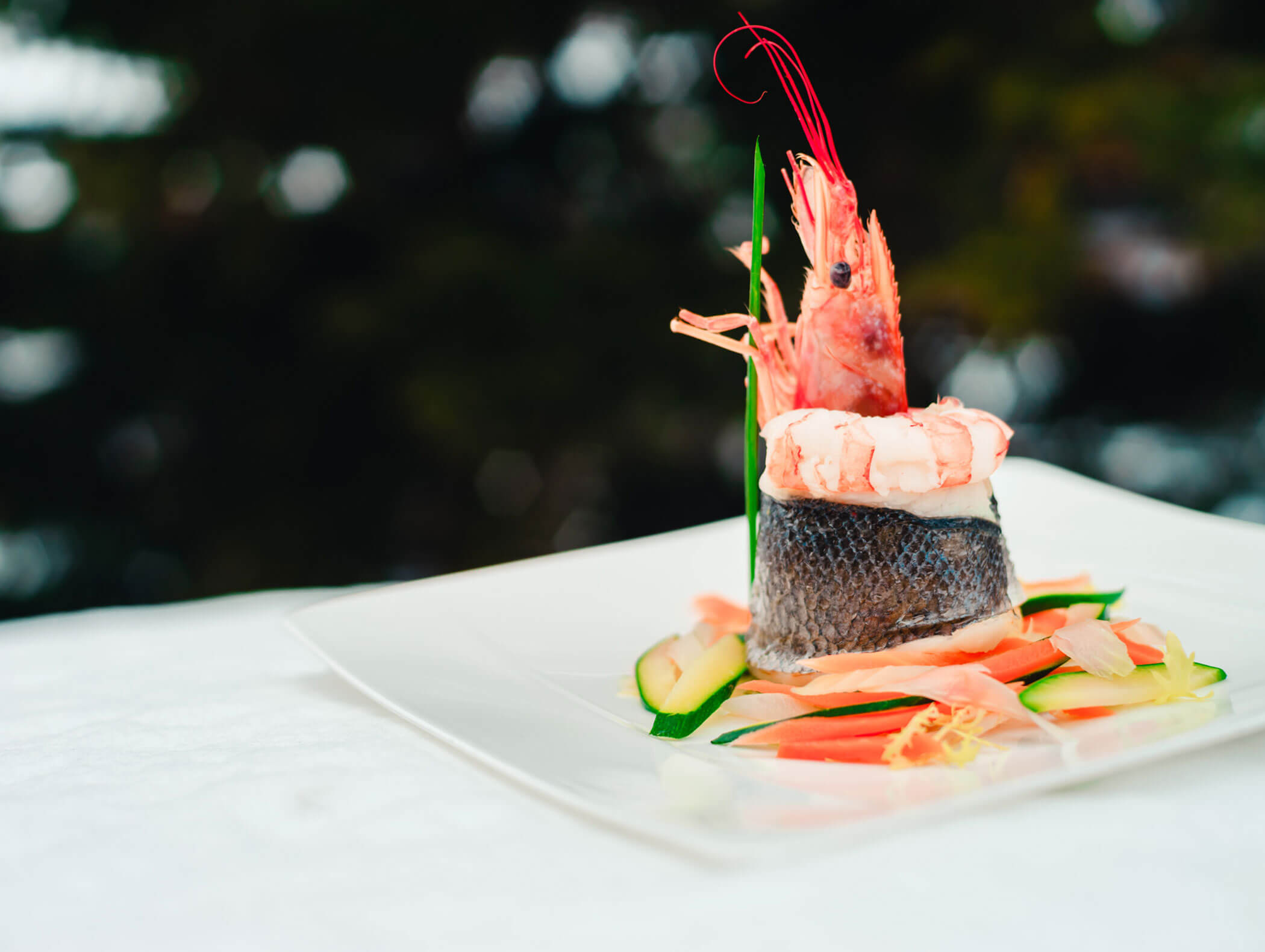 Gourmet seafood dish with shrimp and fish on a bed of sliced vegetables, served on a white plate. - Hotel Kristiania