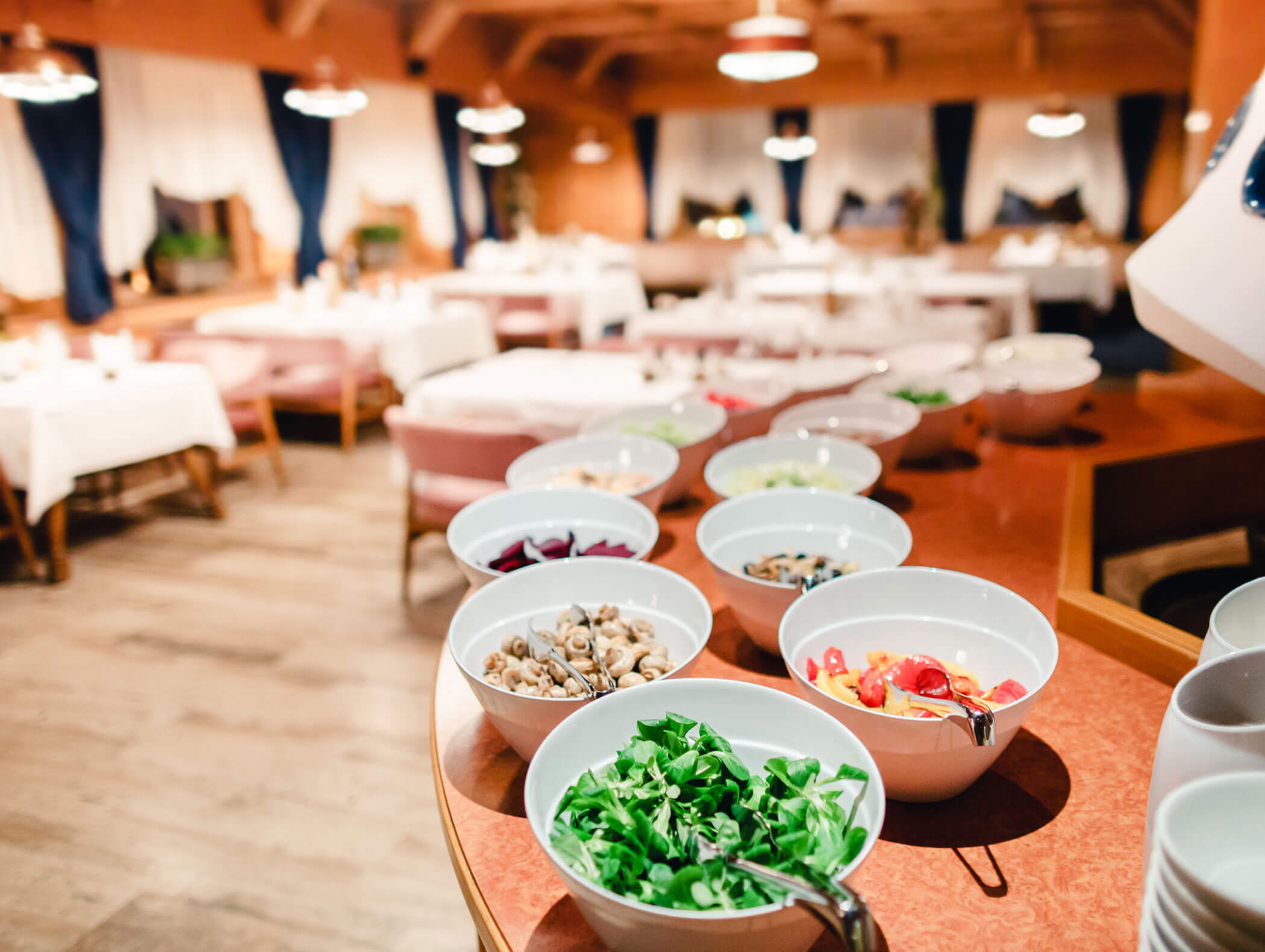 A variety of salads and toppings in bowls are arranged on a counter in a restaurant dining area. - Hotel Kristiania