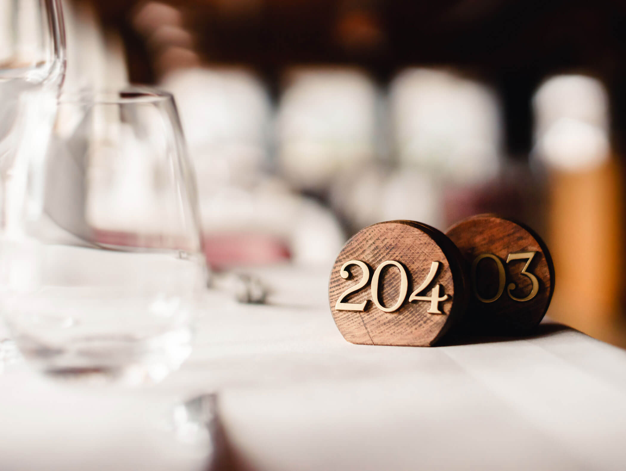 Close-up of a wooden table number holder displaying 204 and 03 on a white tablecloth with glassware. - Hotel Kristiania