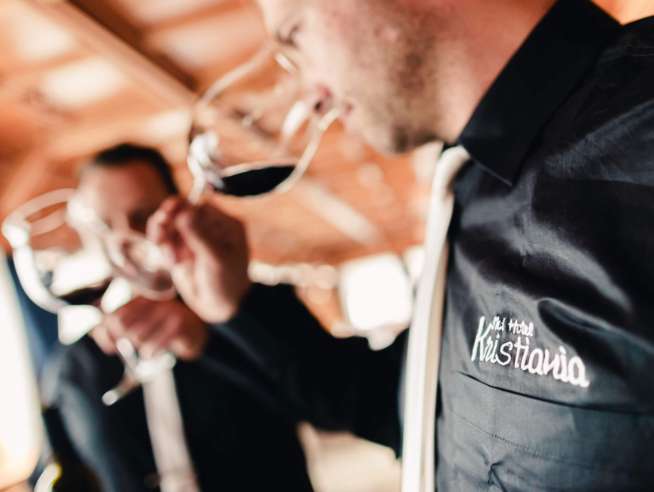 Two people in black shirts swirl and smell red wine in glasses, focusing on aroma, in a warm indoor setting. - Hotel Kristiania