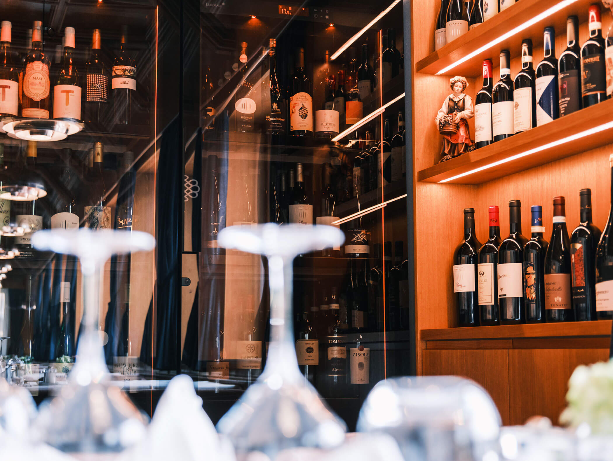 Wine bottles displayed on wooden shelves in a bar, with upside-down glasses in the foreground. - Hotel Kristiania