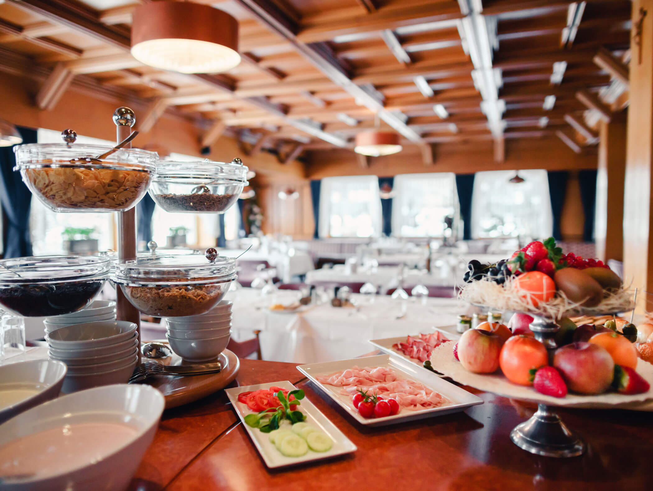 Elegant restaurant with a breakfast buffet, featuring fruits, cereals, and cold cuts on a wooden counter. - Hotel Kristiania