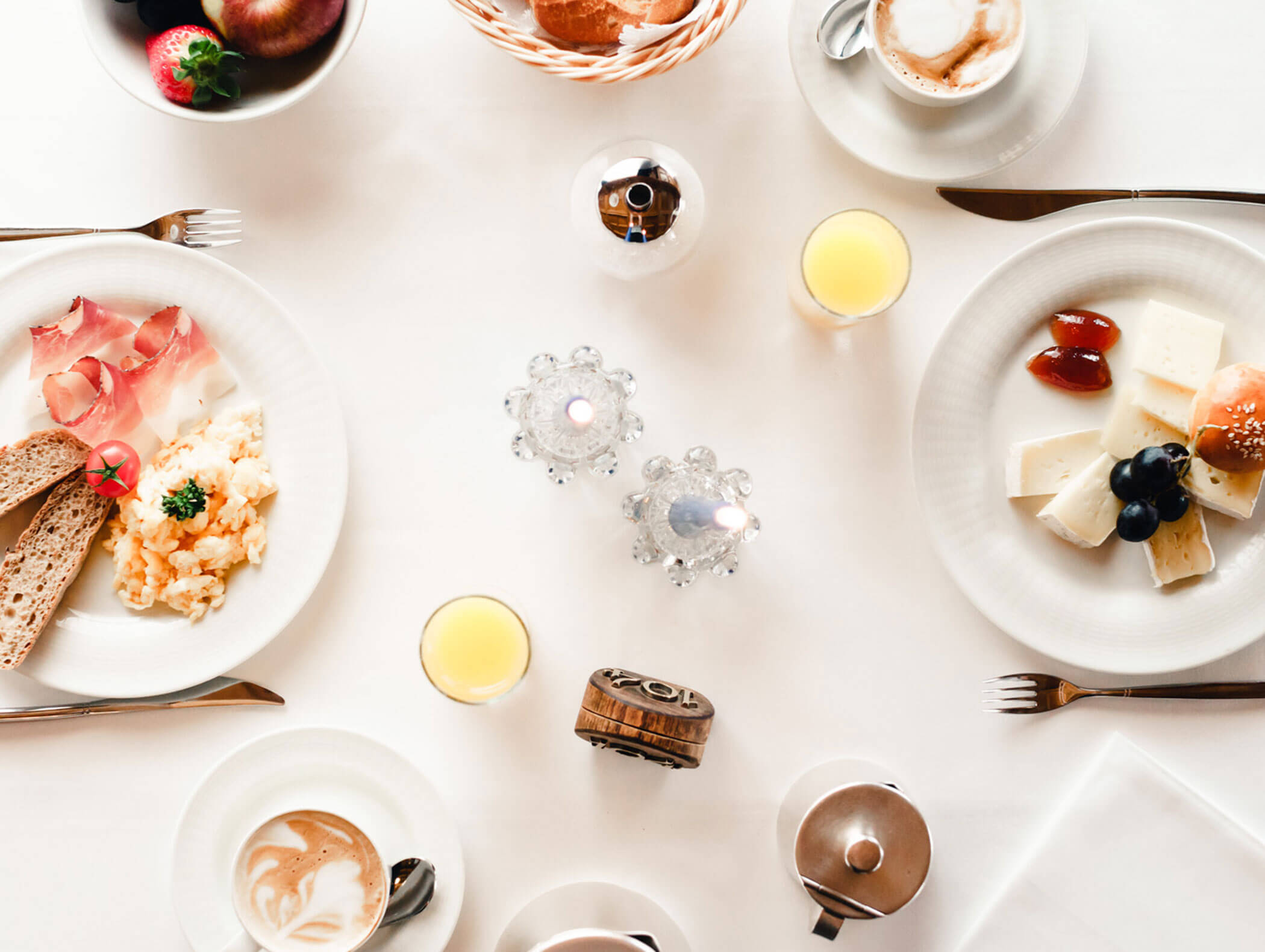 Breakfast table with eggs, bread, cheese, fruit, juice, coffee, and decorative candles on a white tablecloth. - Hotel Kristiania