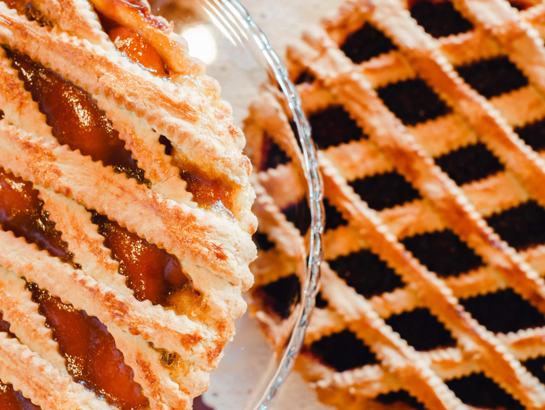 Two lattice-topped pies on a table, one with a golden crust and fruit filling, the other with a dark filling. - Hotel Kristiania