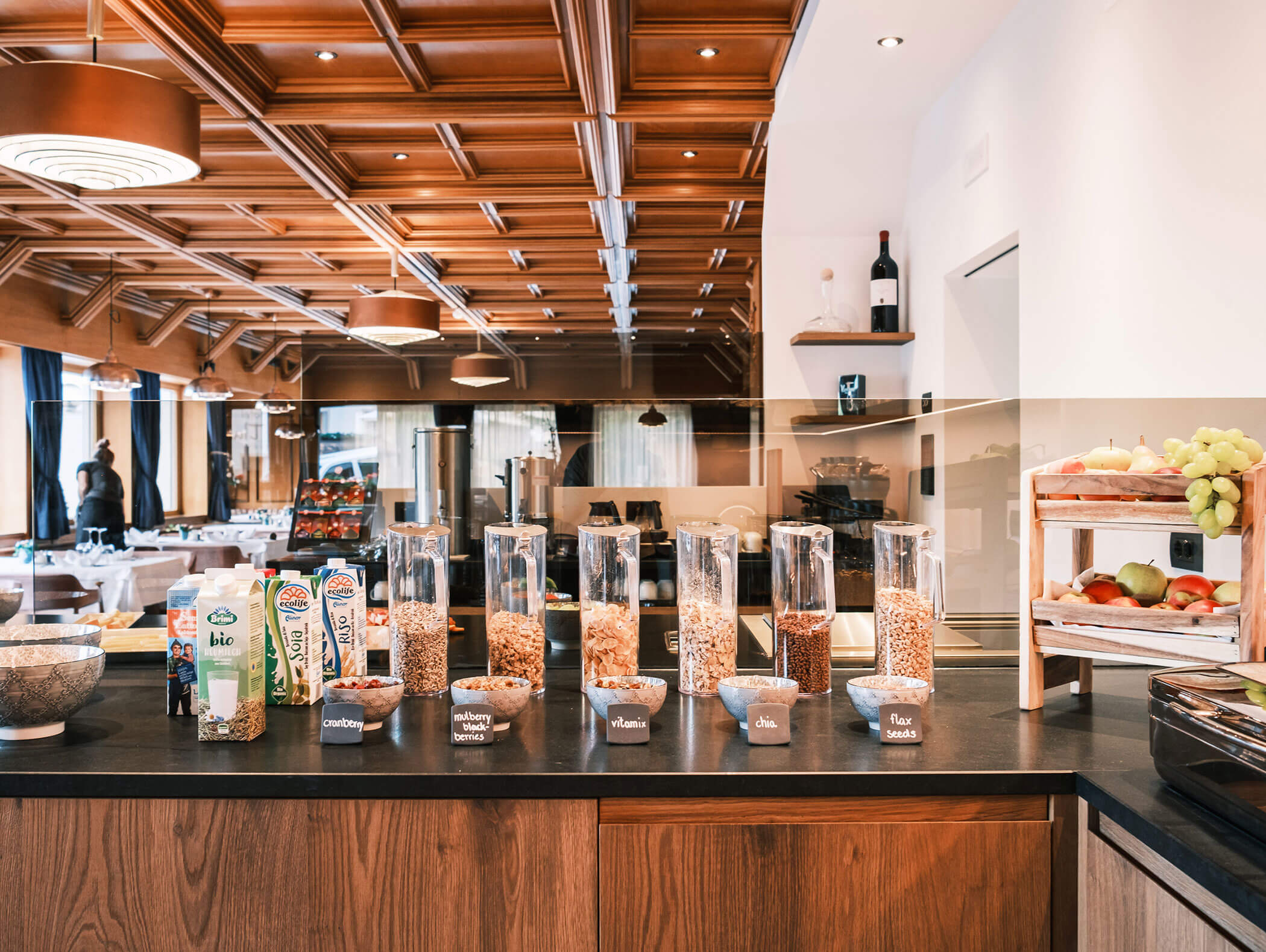 A breakfast buffet with cereal dispensers, milk cartons, fruit, and bowls on a wooden counter in a modern dining area. - Hotel Kristiania