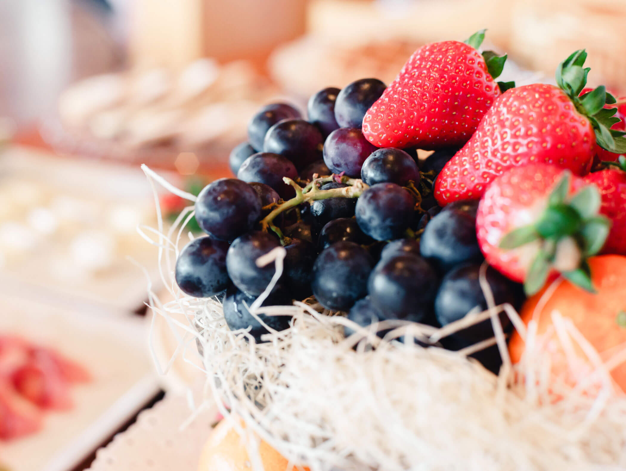 Close-up of fresh strawberries and dark grapes arranged in a basket with straw-like decorative material. - Hotel Kristiania