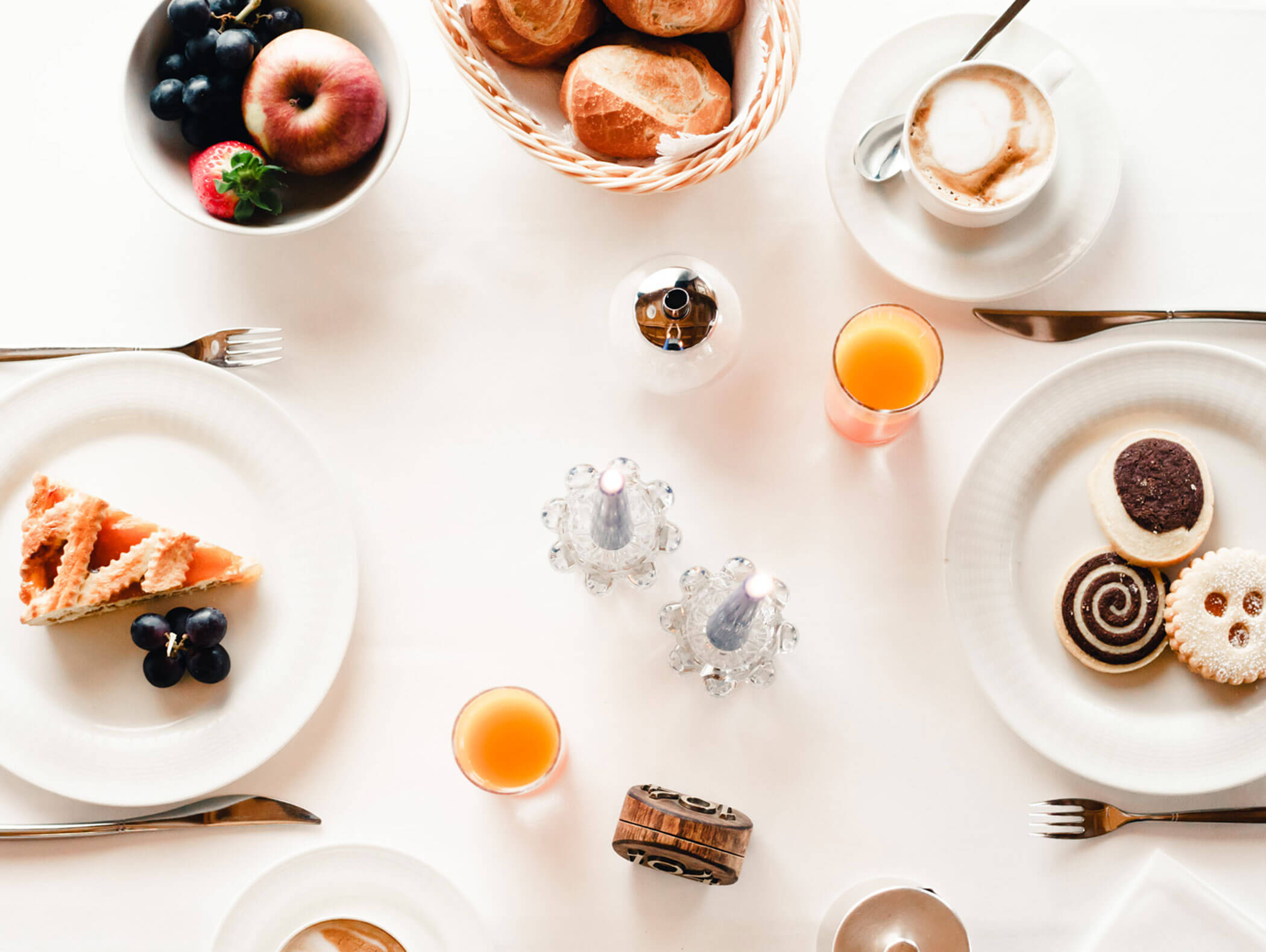 Breakfast table with pastries, cookies, fruit, bread rolls, orange juice, and coffee on white dishes. - Hotel Kristiania