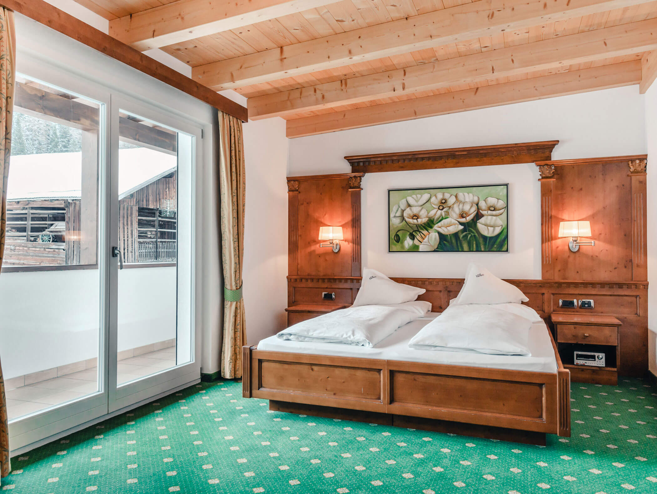 Accogliente camera d'albergo con letto matrimoniale, arredi in legno, moquette verde e ampia finestra che si affaccia su un balcone. - Hotel Kristiania