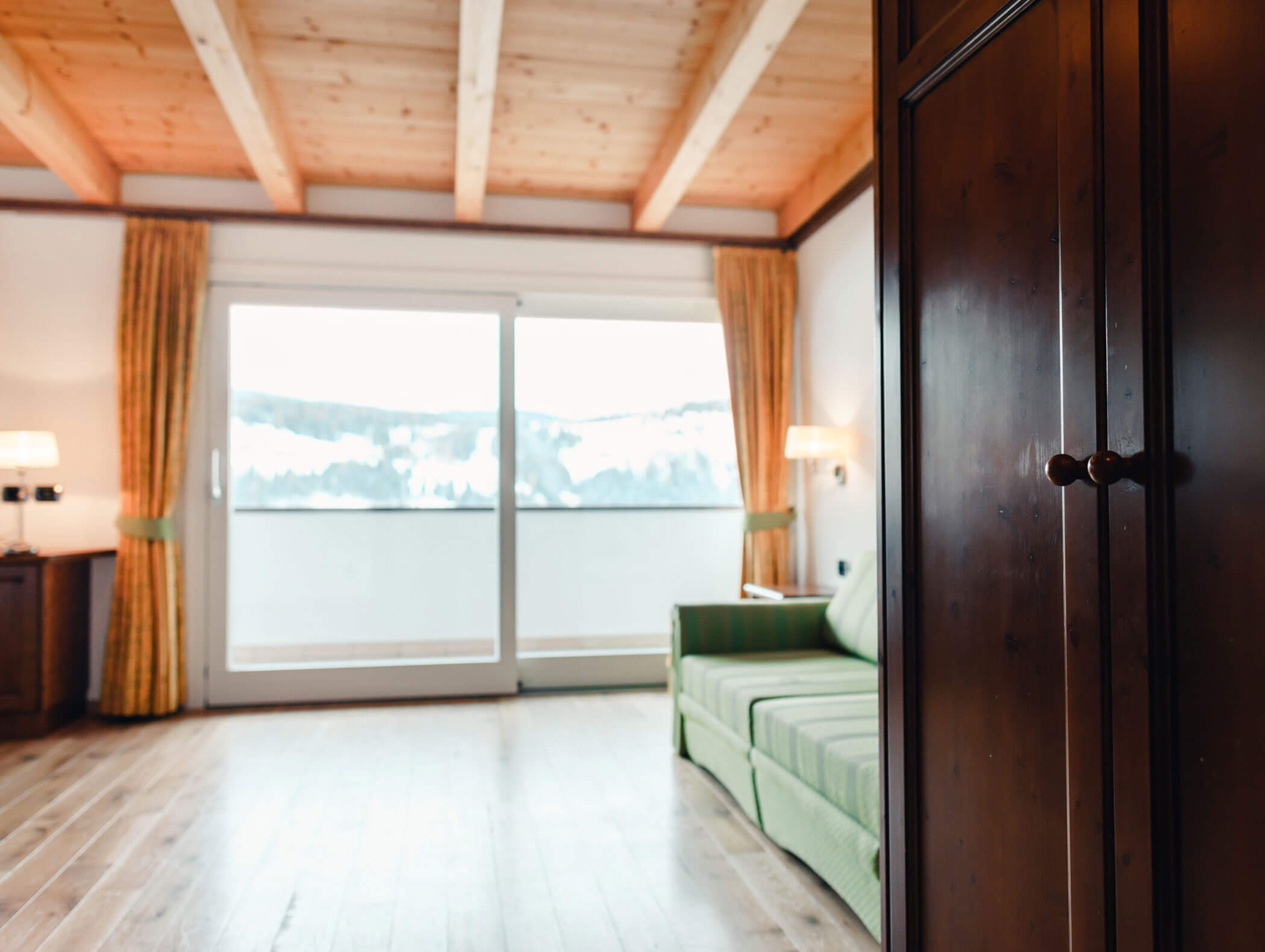 Stanza luminosa con soffitto in legno, divano verde, ampia finestra e armadio in primo piano. - Hotel Kristiania