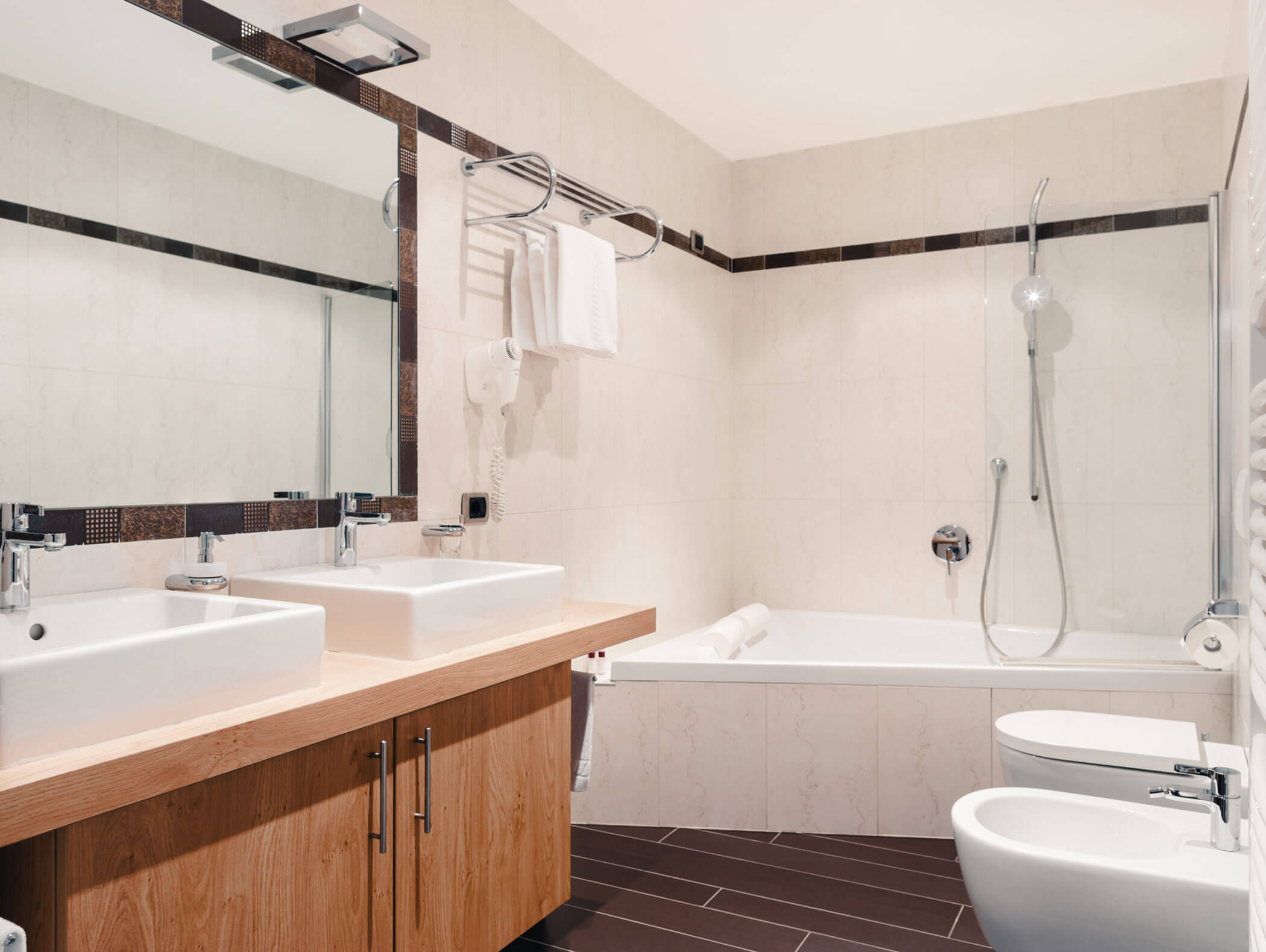 Bagno moderno con doppio lavabo, ampio specchio, vasca da bagno con doccia, bidet e portasciugamani sopra. - Hotel Kristiania