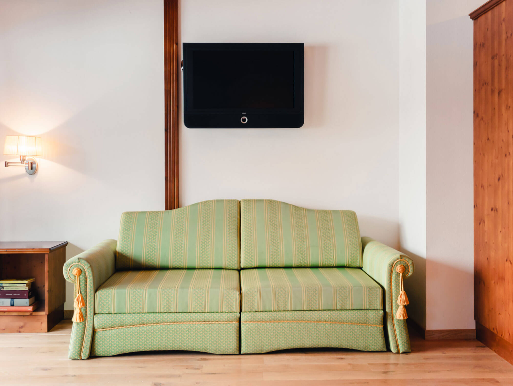 Divano imbottito verde sotto una TV a parete in un soggiorno luminoso e minimalista con dettagli in legno. - Hotel Kristiania