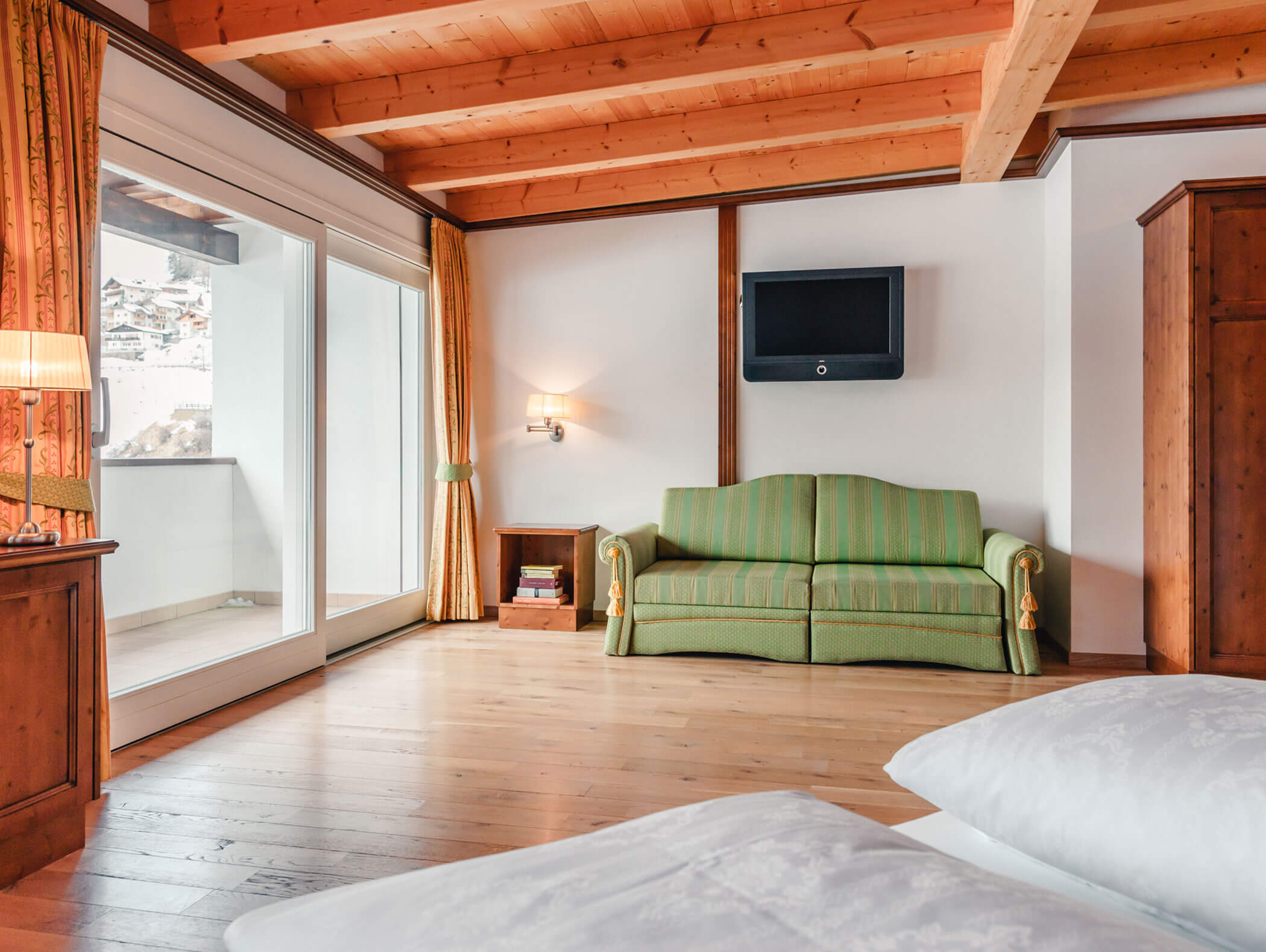 Una camera d'albergo accogliente con un divano verde, mobili in legno, TV e un balcone con vista sulle montagne. - Hotel Kristiania