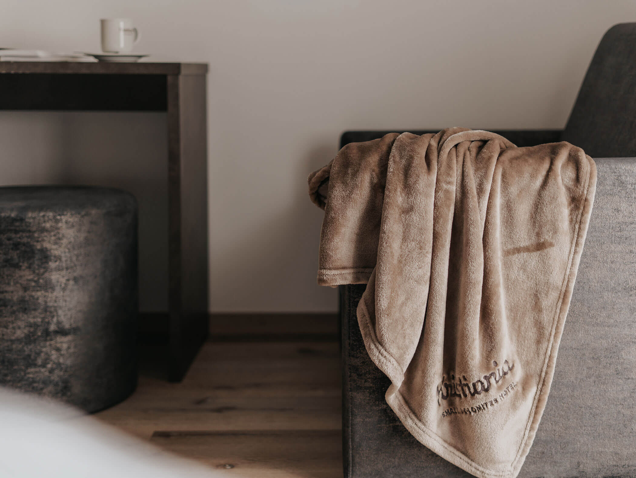 Una coperta marrone appoggiata su una sedia grigia, accanto a un tavolino scuro con una tazza e un piattino. - Hotel Kristiania