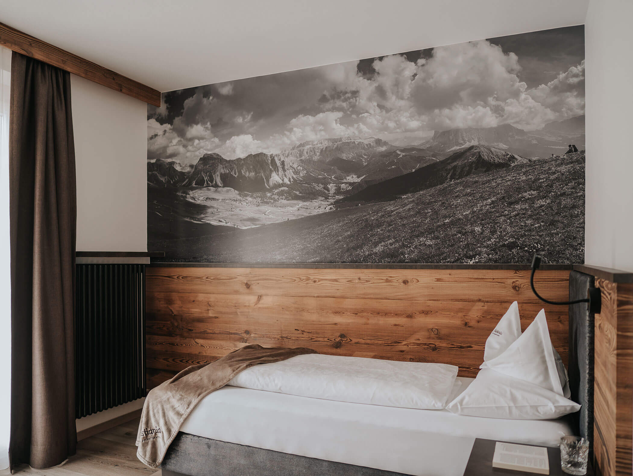 Un letto singolo con lenzuola bianche accanto a un murale raffigurante delle montagne, in una stanza moderna e minimalista. - Hotel Kristiania