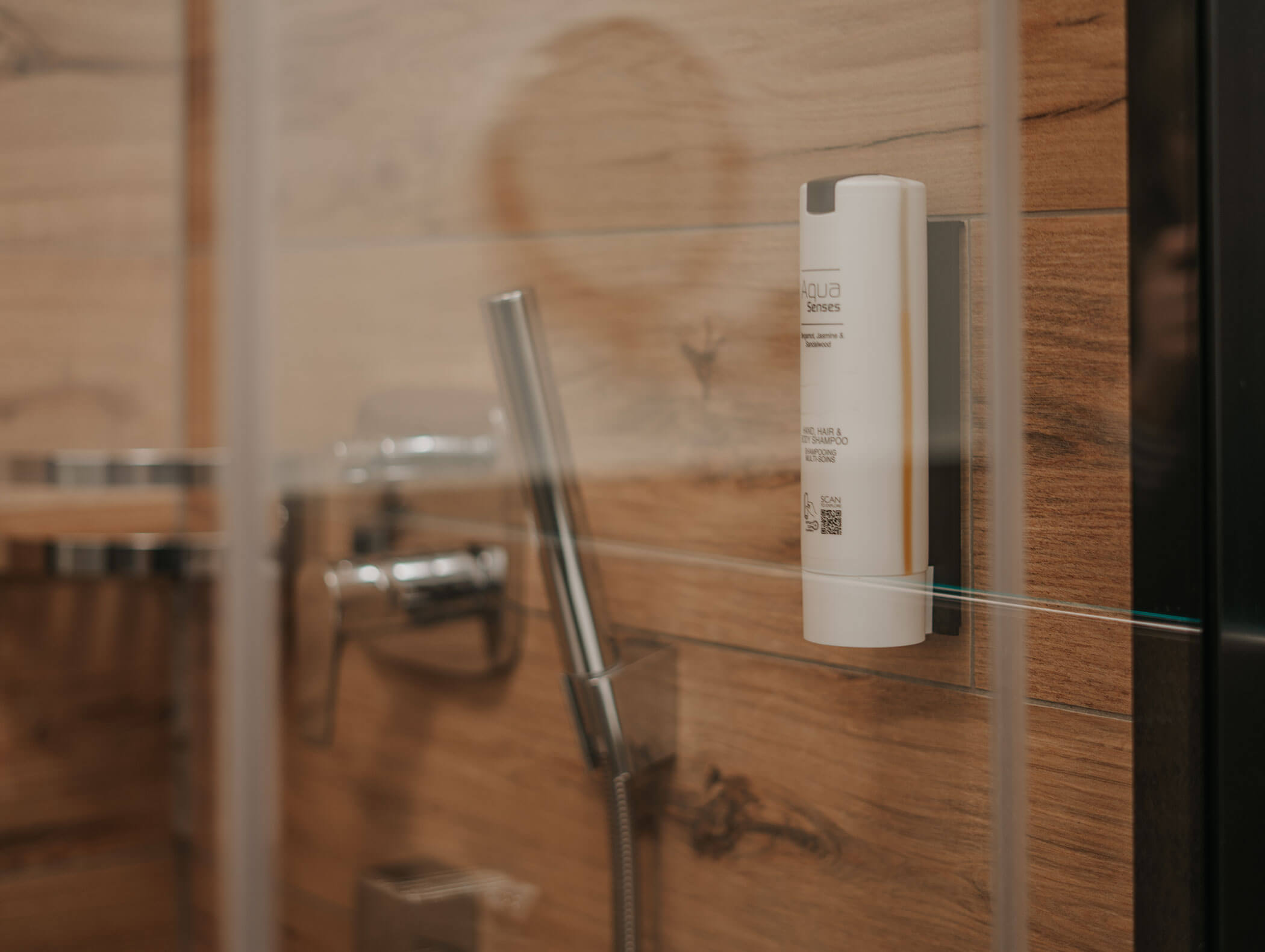 Doccia con parete effetto legno, rubinetteria in metallo e un dispenser per sapone bianco fissato su una lastra di vetro. - Hotel Kristiania