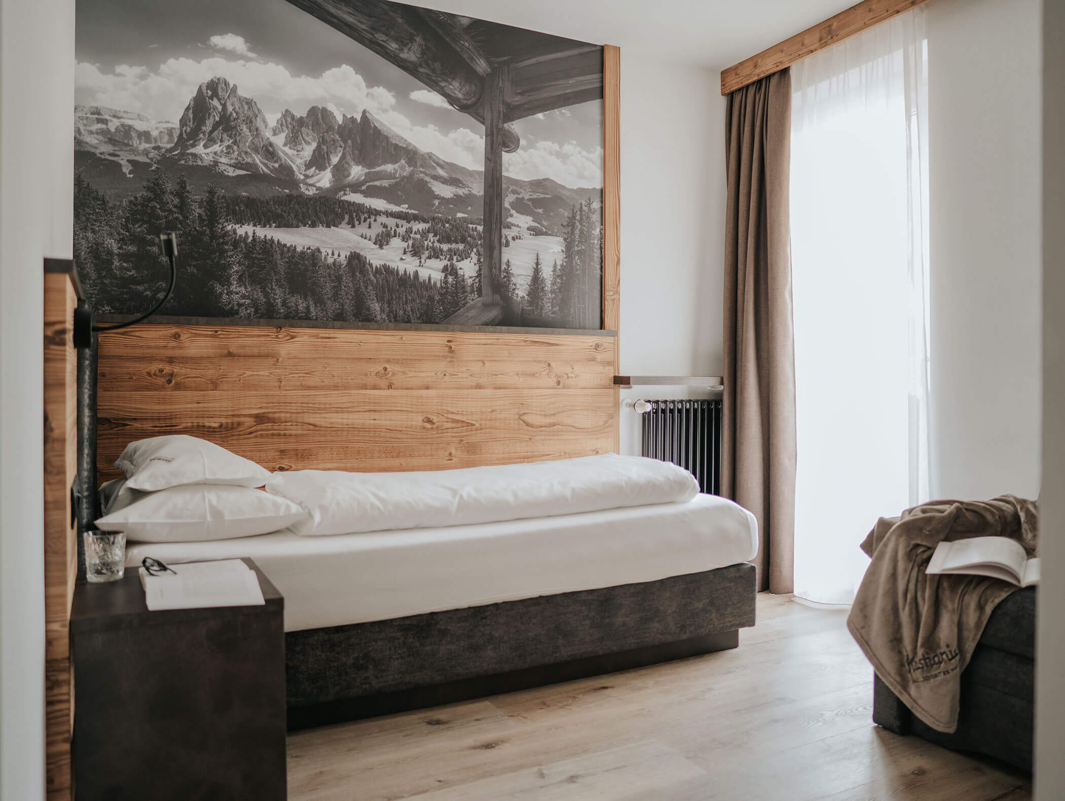 Una camera da letto accogliente con un letto singolo, dettagli in legno e un grande murale con un paesaggio montano sopra la testiera. - Hotel Kristiania