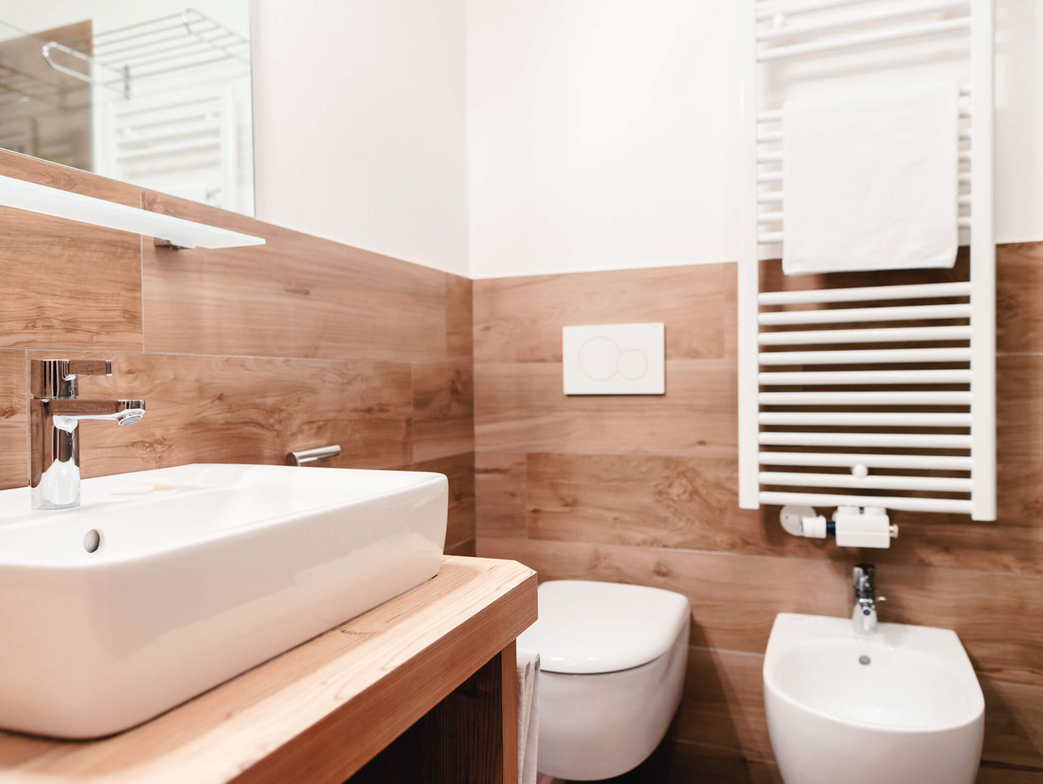 Bagno moderno con lavabo bianco, WC, bidet, dettagli in legno e uno scaldasalviette a parete. - Hotel Kristiania