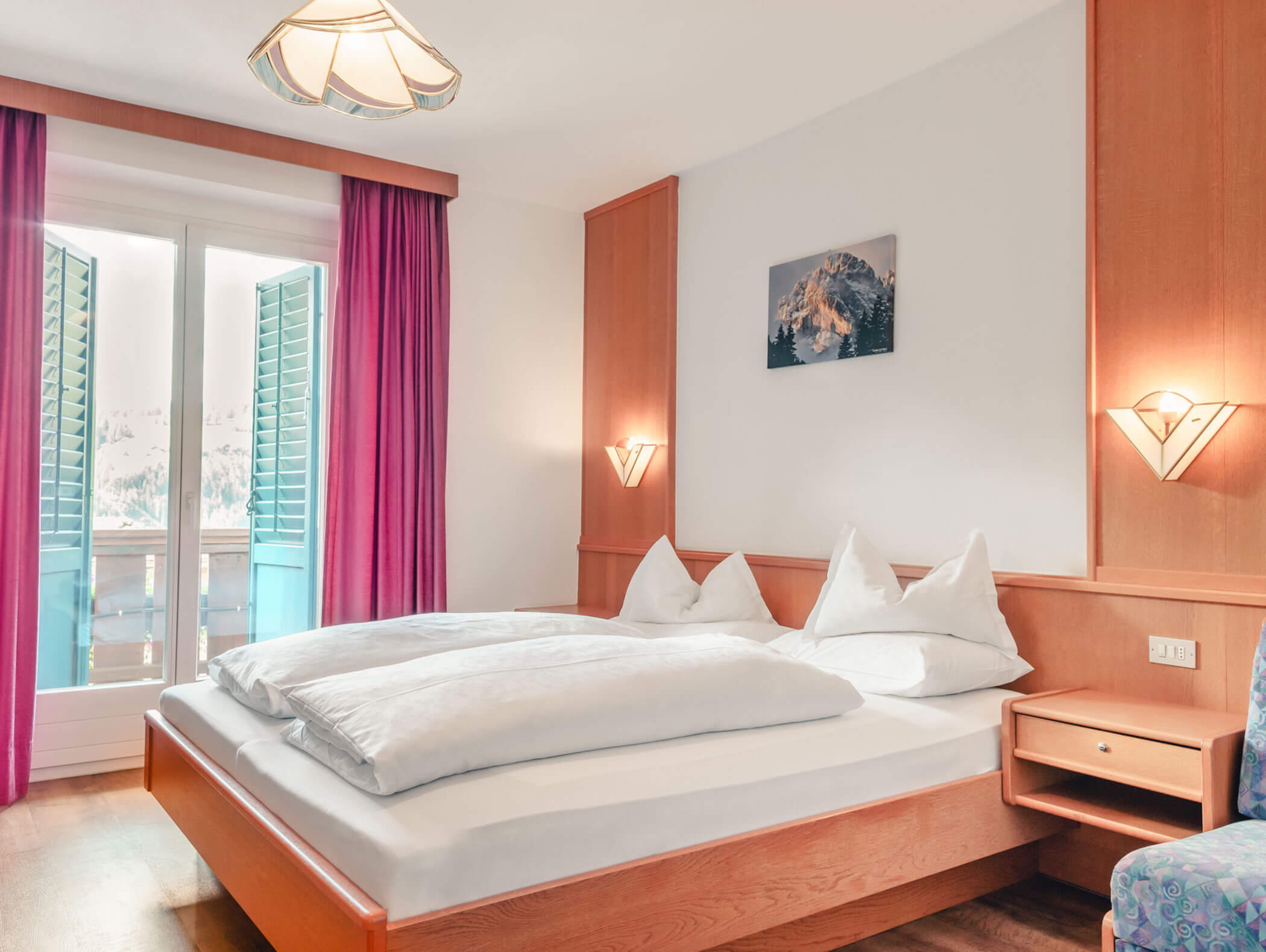Camera d'albergo luminosa con letto matrimoniale, mobili in legno, tende rosa e persiane aperte. - Hotel Kristiania