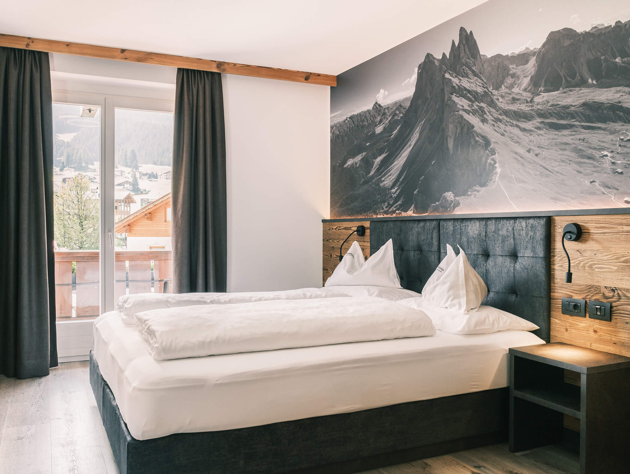Camera d'albergo luminosa con letto matrimoniale, un grande murale raffigurante una montagna e portefinestre che si affacciano su un panorama mozzafiato. - Hotel Kristiania