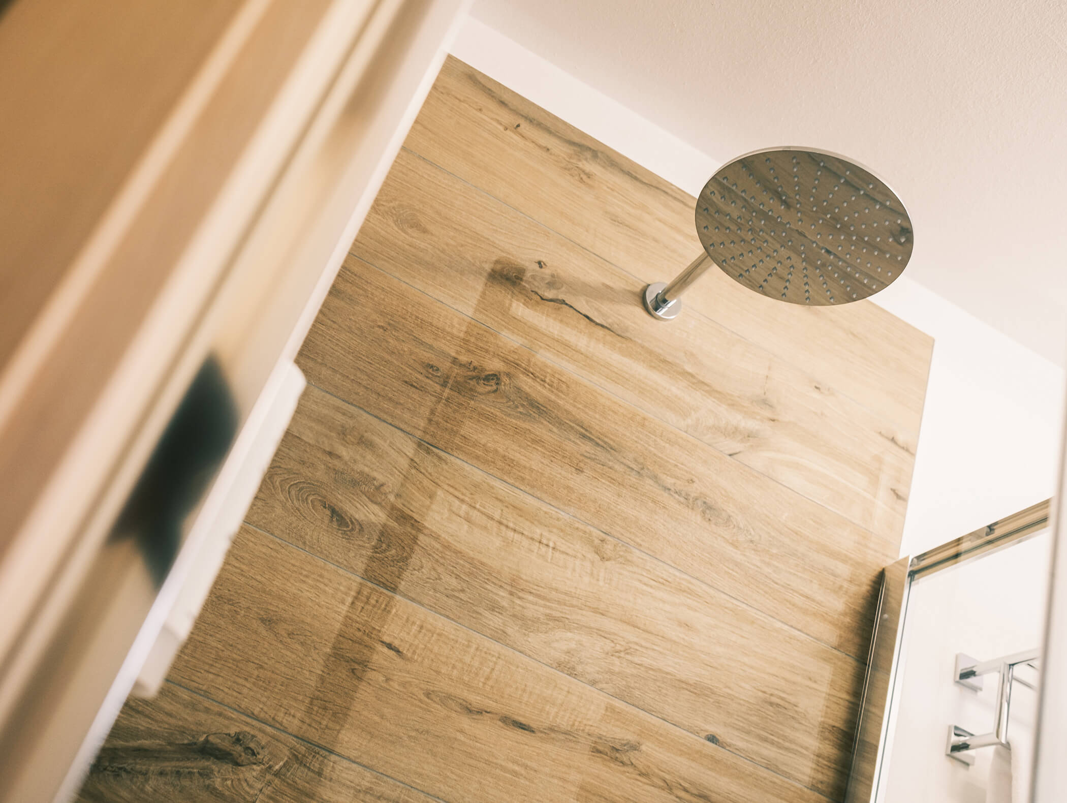 Soffione rotondo a soffitto sopra una doccia con piastrelle effetto legno e rubinetteria moderna. - Hotel Kristiania