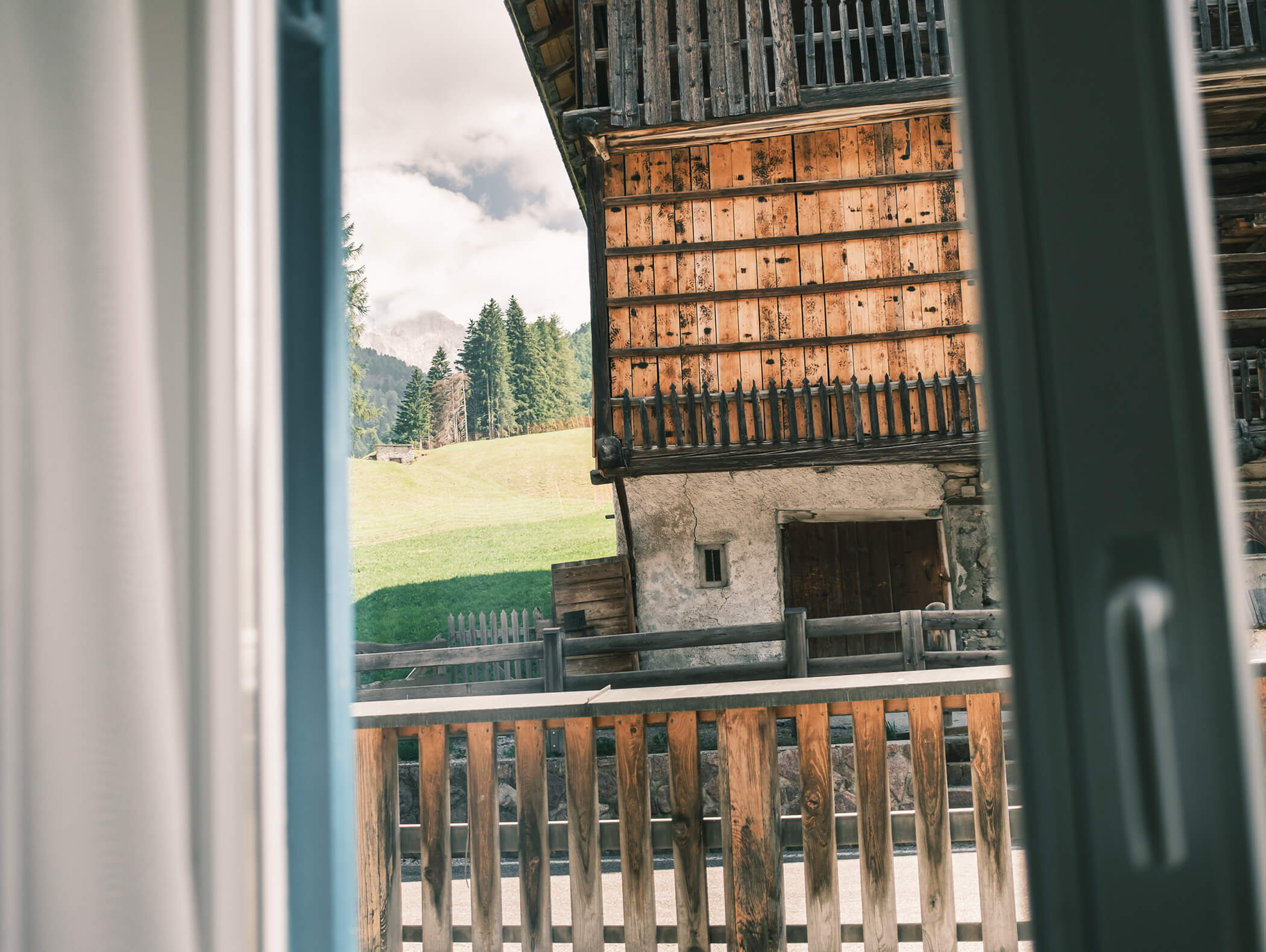 Vista attraverso una finestra aperta di una baita di legno, la ringhiera del balcone e un pendio verde con alberi. - Hotel Kristiania