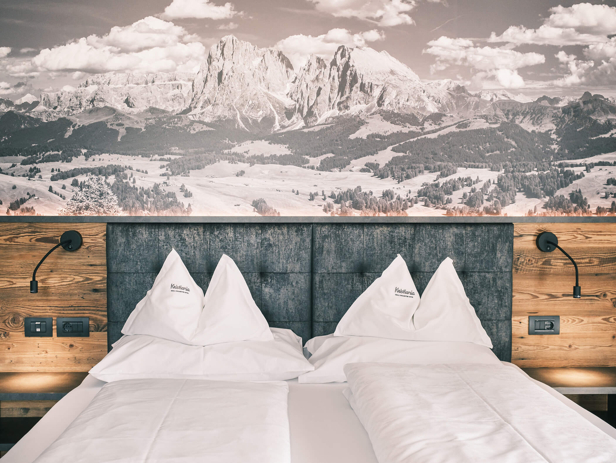 Un accogliente letto d'albergo con lenzuola bianche, dettagli in legno e un grande murale raffigurante un paesaggio montano sulla parete alle sue spalle. - Hotel Kristiania