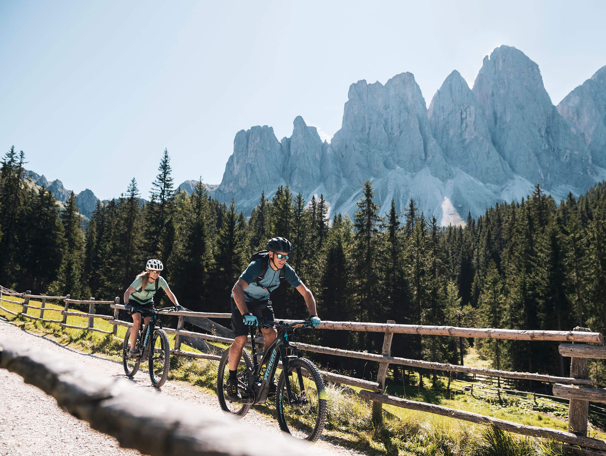 Zwei Menschen fahren mit dem Mountainbike auf einem Feldweg, im Hintergrund sind Kiefern und felsige Berge zu sehen. - Hotel Kristiania