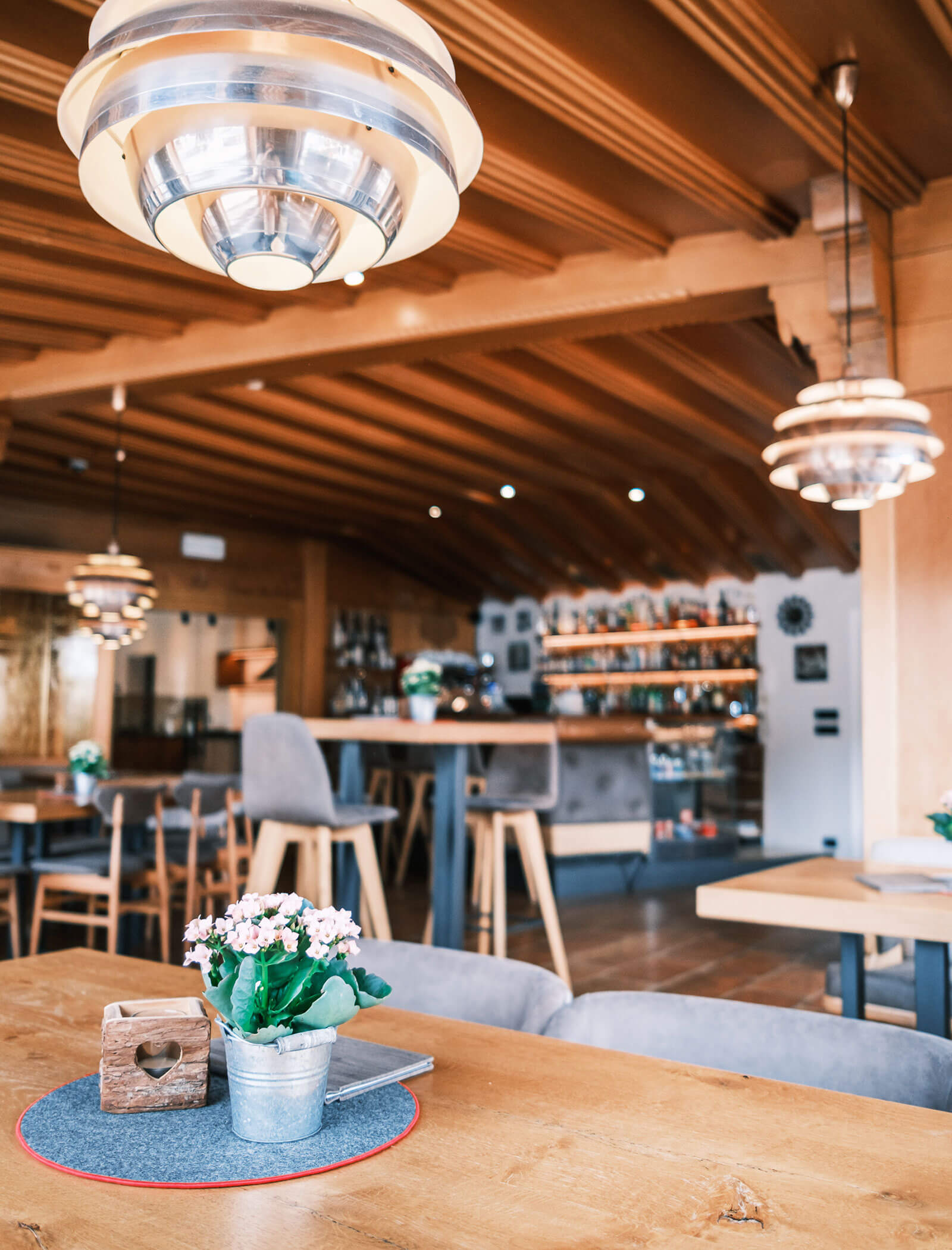 Gemütliches Restaurantinterieur mit Holztischen, moderner Beleuchtung und Blumen in einem Topf auf dem Tisch. - Hotel Kristiania