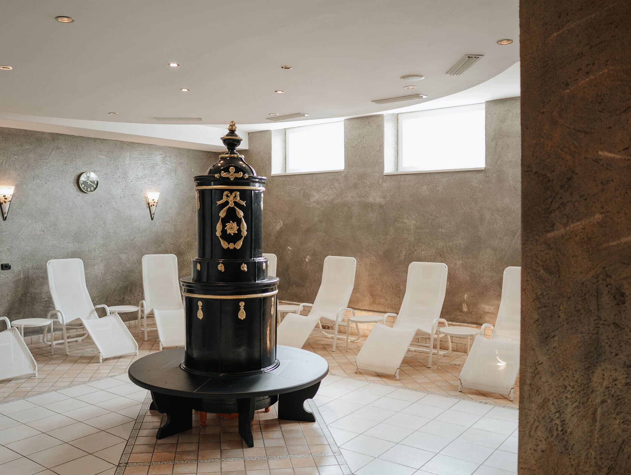 Ein runder Raum mit weißen Liegestühlen und einem schwarzen Zierofen in der Mitte, beleuchtet von sanfter Beleuchtung. - Hotel Kristiania