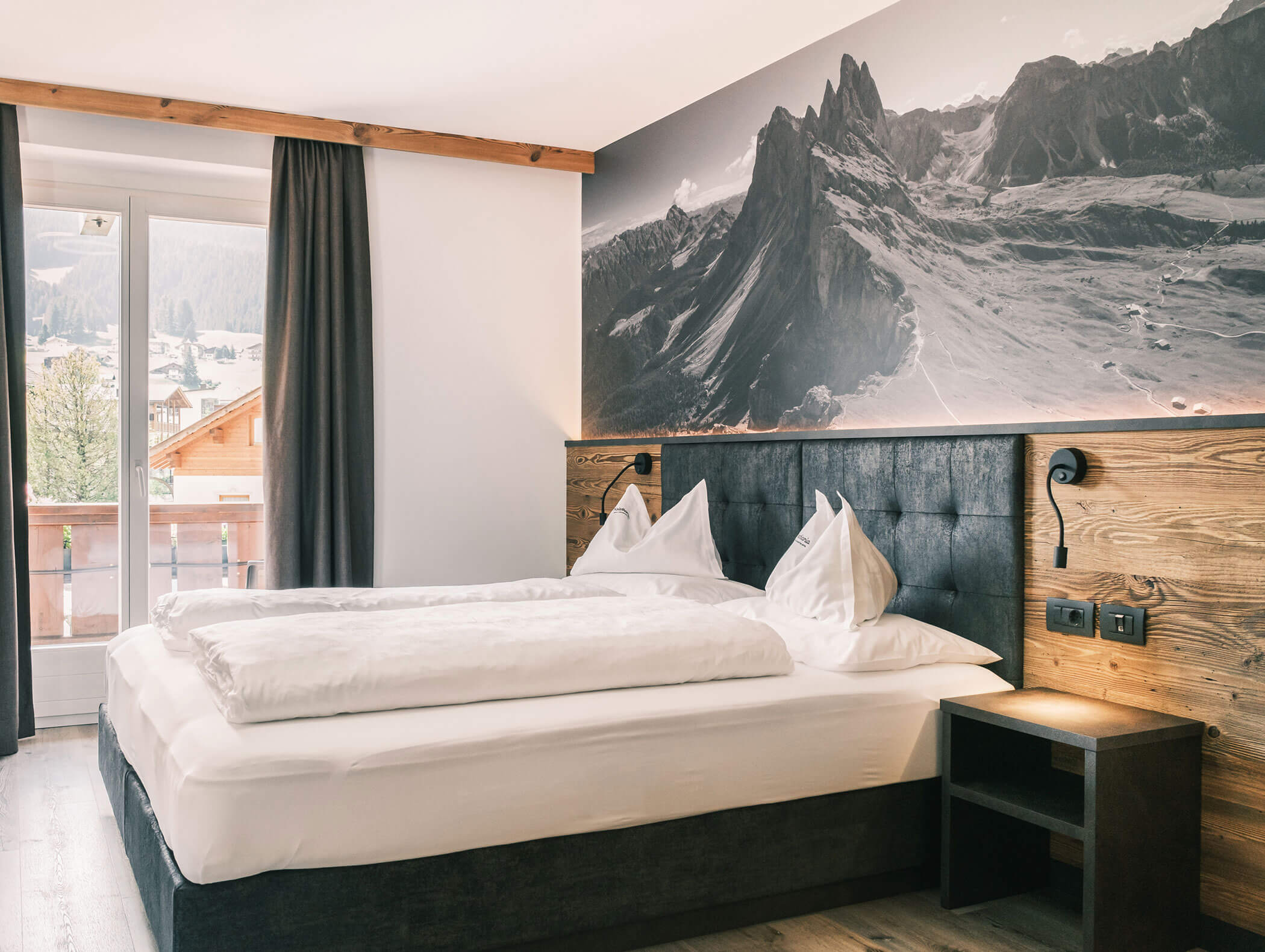 Modernes Hotelzimmer mit einem Doppelbett, einem Wandbild mit Bergmotiv, einem Balkon und einem großen Fenster mit Vorhängen. - Hotel Kristiania