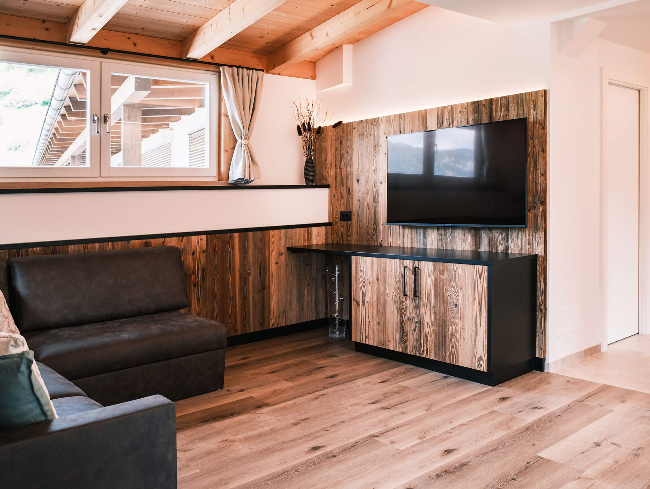 Soggiorno moderno con dettagli in legno, un divano grigio, una TV a schermo piatto e un'ampia finestra che lascia entrare la luce naturale. - Hotel Kristiania