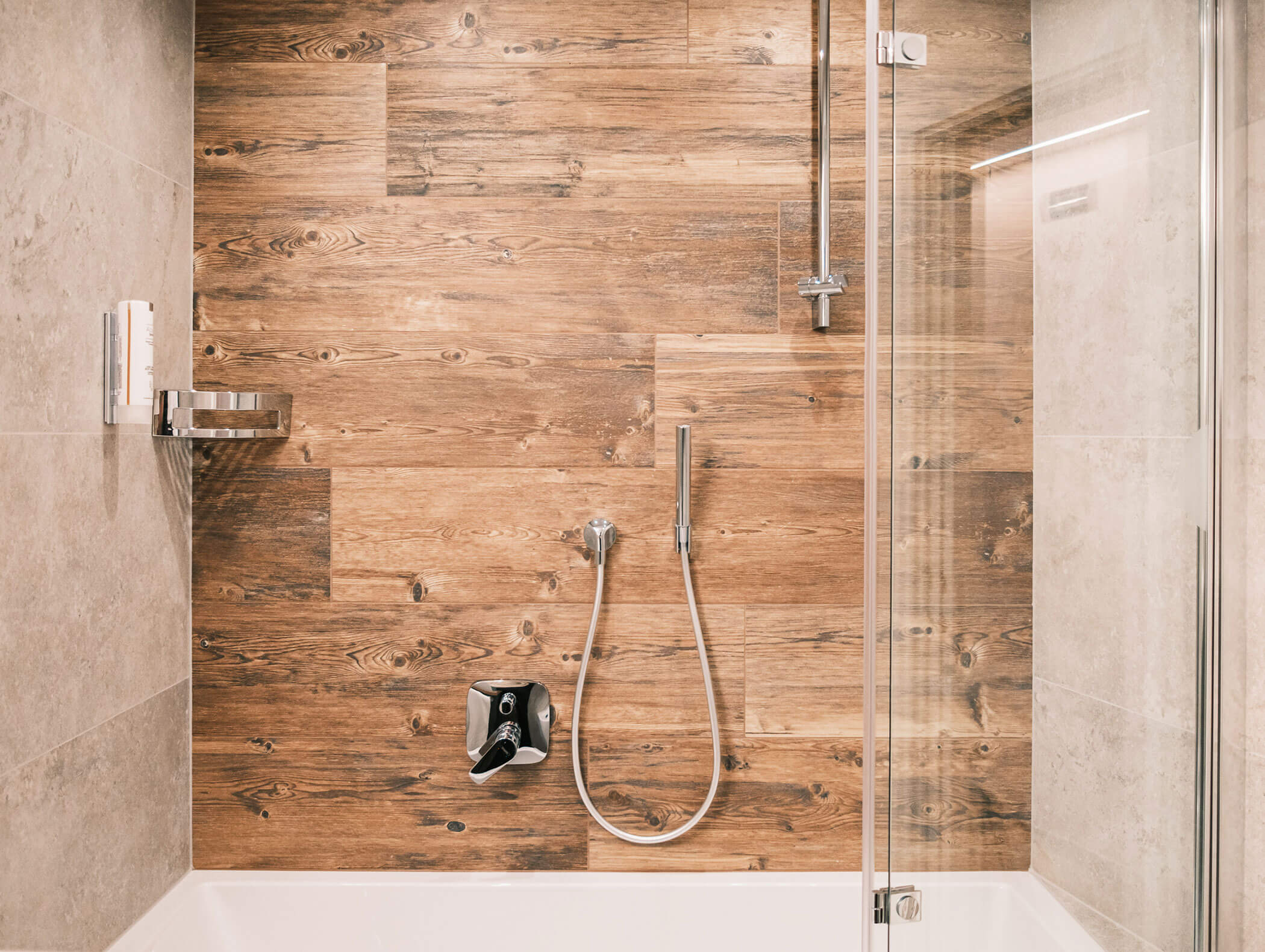 Doccia moderna con piastrelle da rivestimento effetto legno, porta in vetro, mensola a incasso e rubinetteria argentata. - Hotel Kristiania