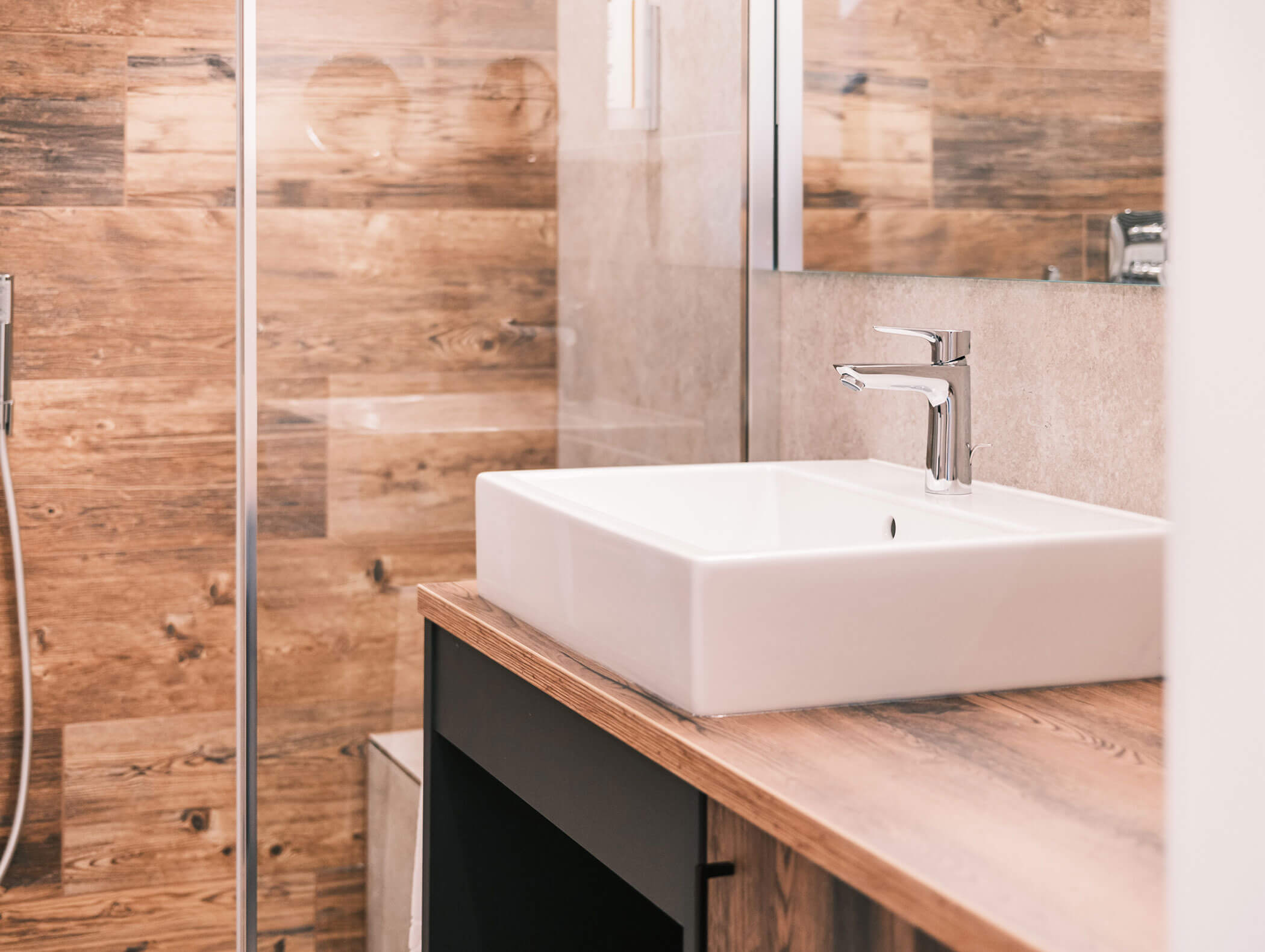 Bagno moderno con lavabo quadrato bianco, piano di appoggio in legno e piastrelle da rivestimento con motivo a legno. - Hotel Kristiania