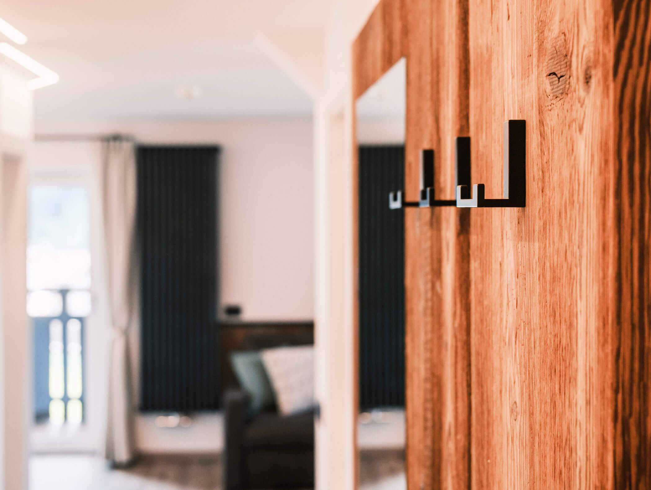 Primo piano di appendiabiti neri su una parete di legno, con un soggiorno sfocato sullo sfondo. - Hotel Kristiania