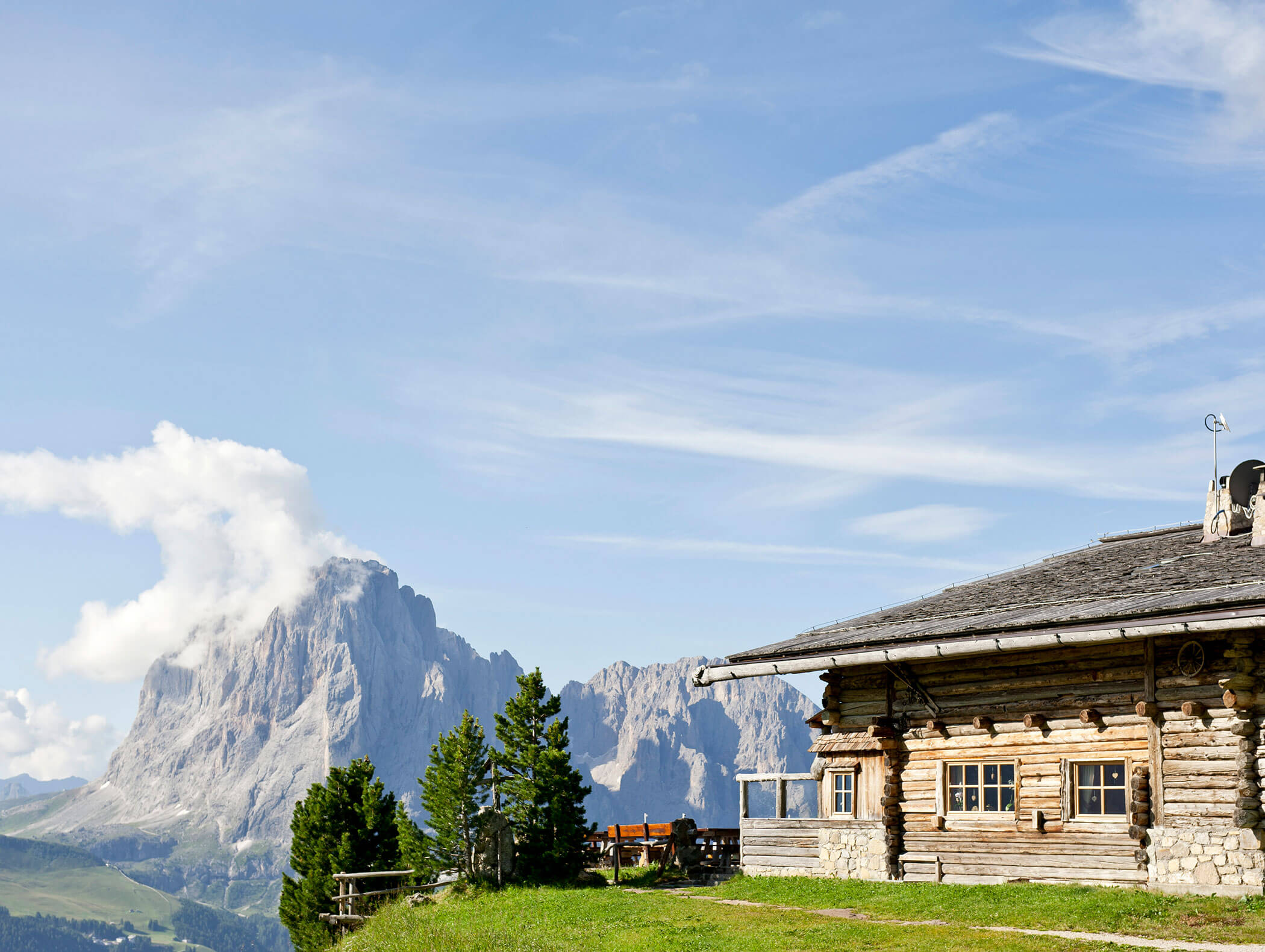 Eine Holzhütte auf einem grasbewachsenen Hügel, im Hintergrund Berge und blauer Himmel. - Hotel Kristiania