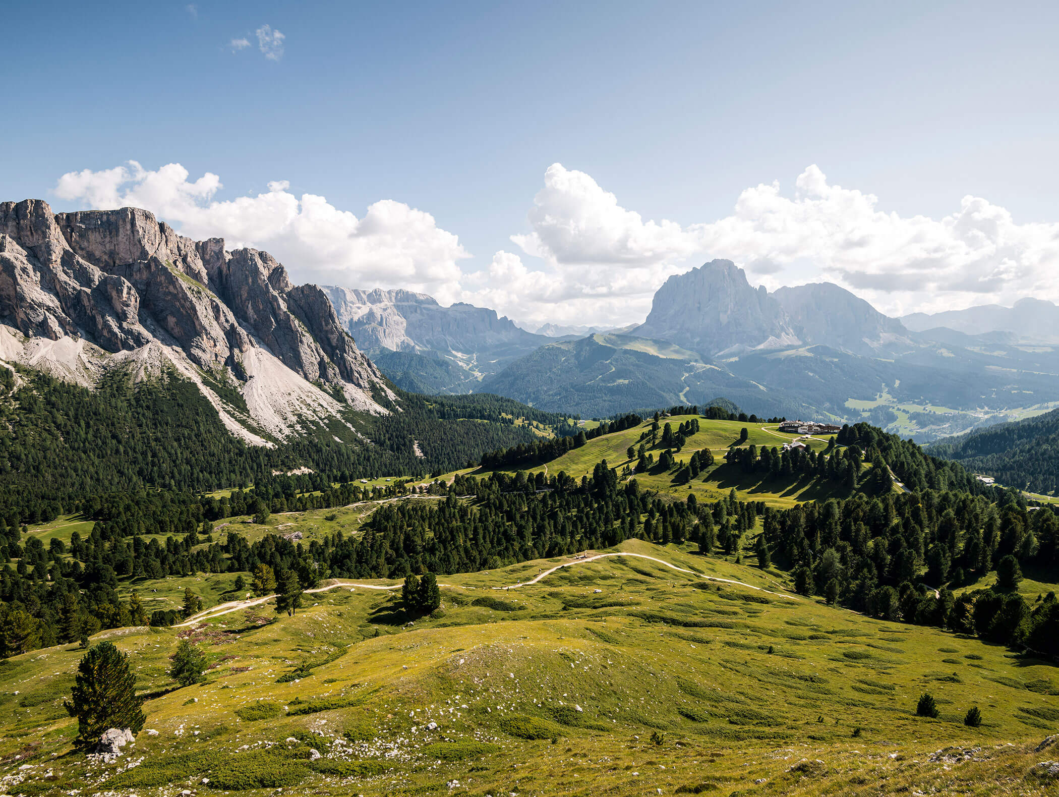 Grüne Hügel und vereinzelte Bäume vor dem Hintergrund von Berggipfeln und blauem Himmel unter vereinzelten Wolken. - Hotel Kristiania